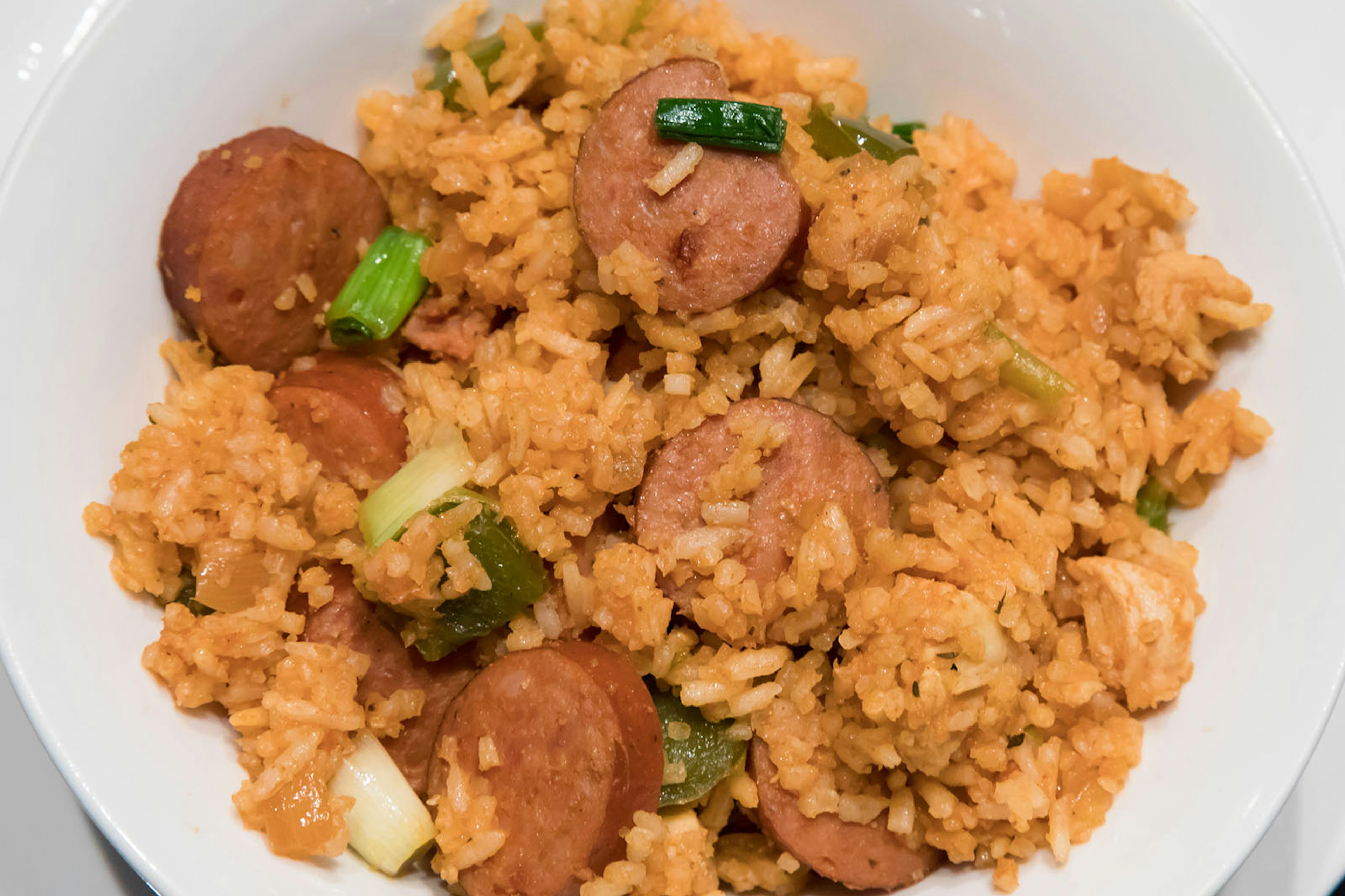 Cajun sausage and rice garnished with green onion (aka jambalaya) served in a plain white bowl © KaraGrubis / Getty Images