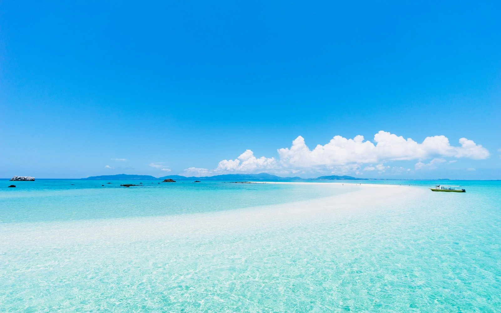 A turquoise blue ocean dotted with spits of land against a pure blue sky with a boat