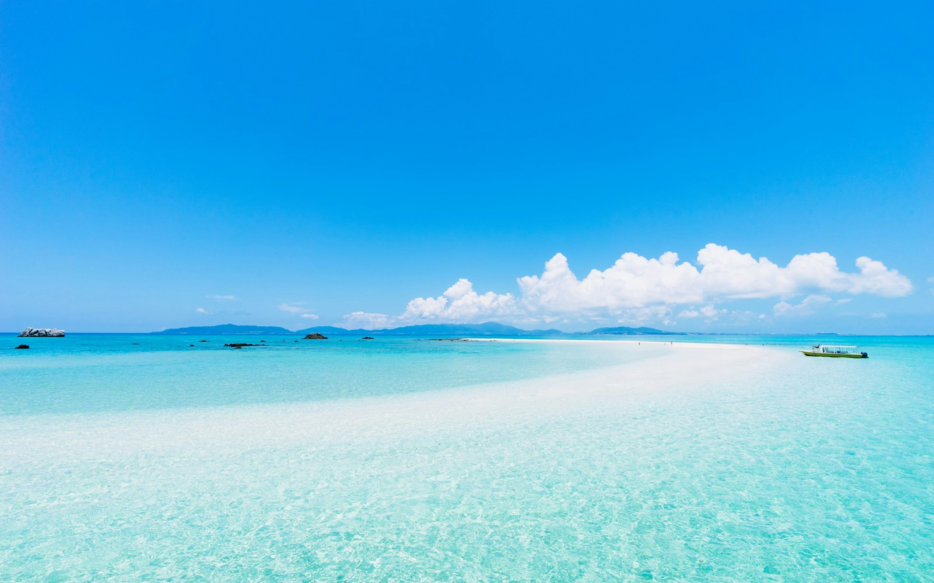 A turquoise blue ocean dotted with spits of land against a pure blue sky with a boat