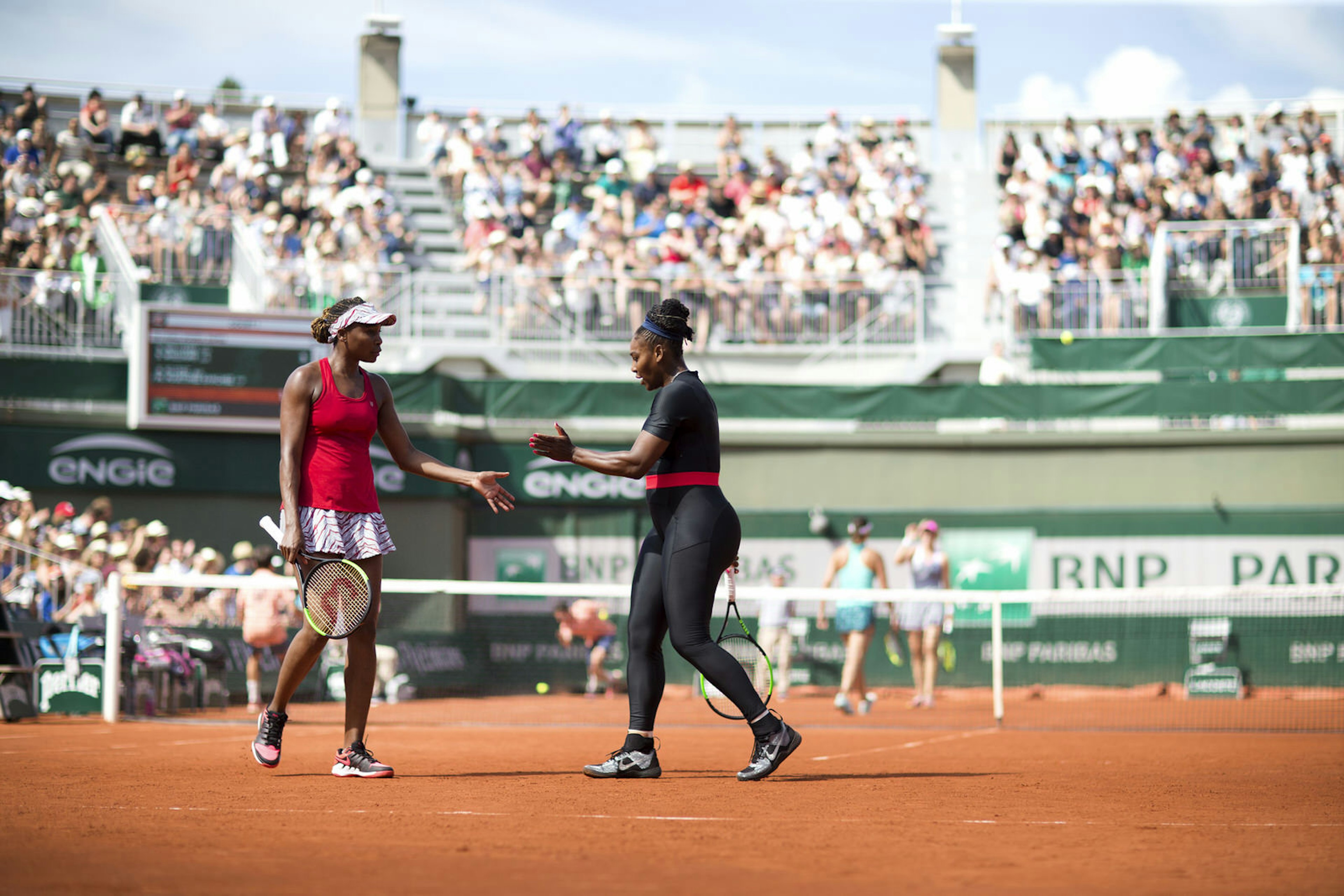 Serena Williams and Venus Williams high-five each other on a clay court at the French Open