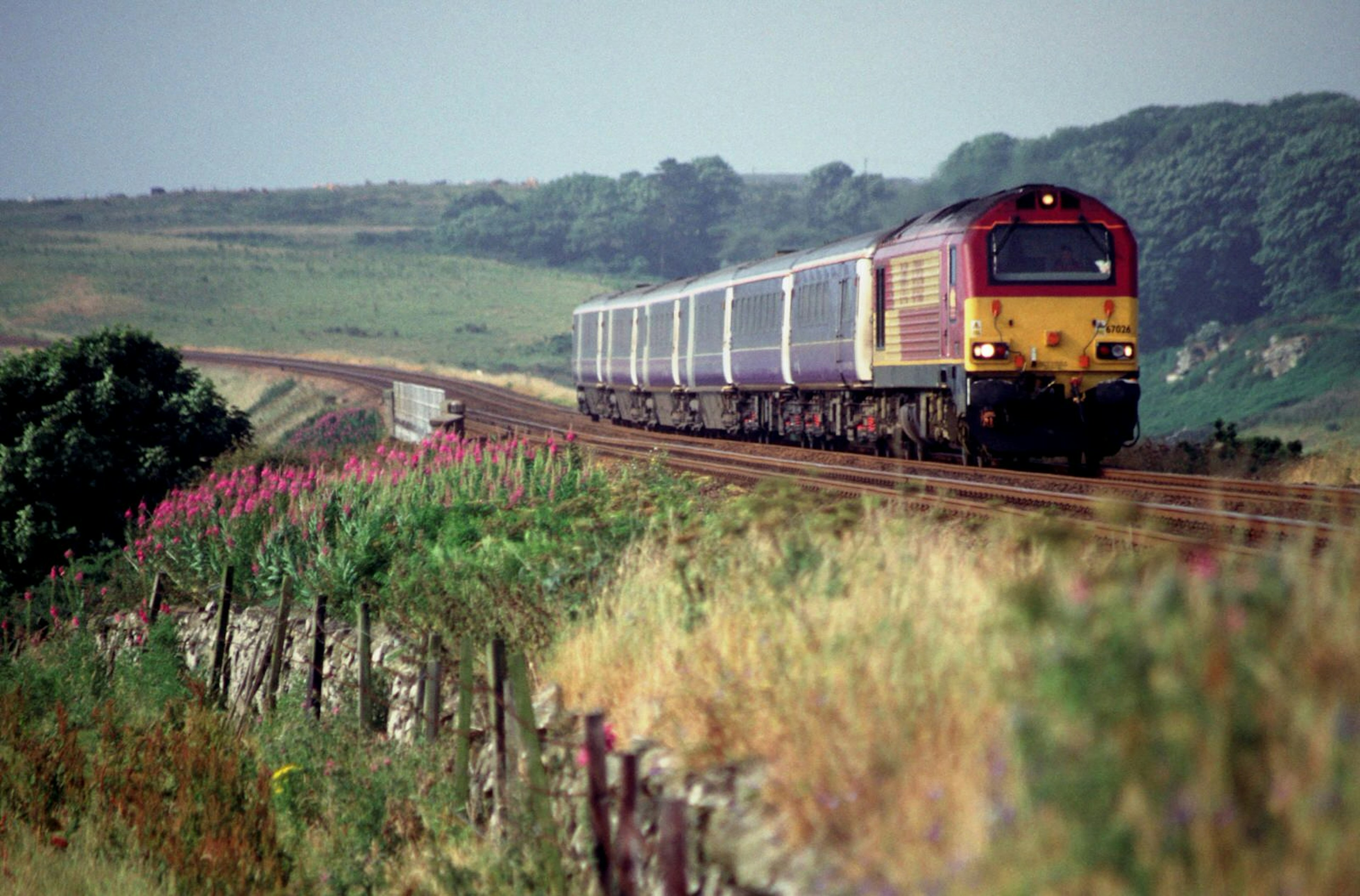 The Caledonian Sleeper rumbles along a section of track in Scotland with wide green fields located on either side of the track