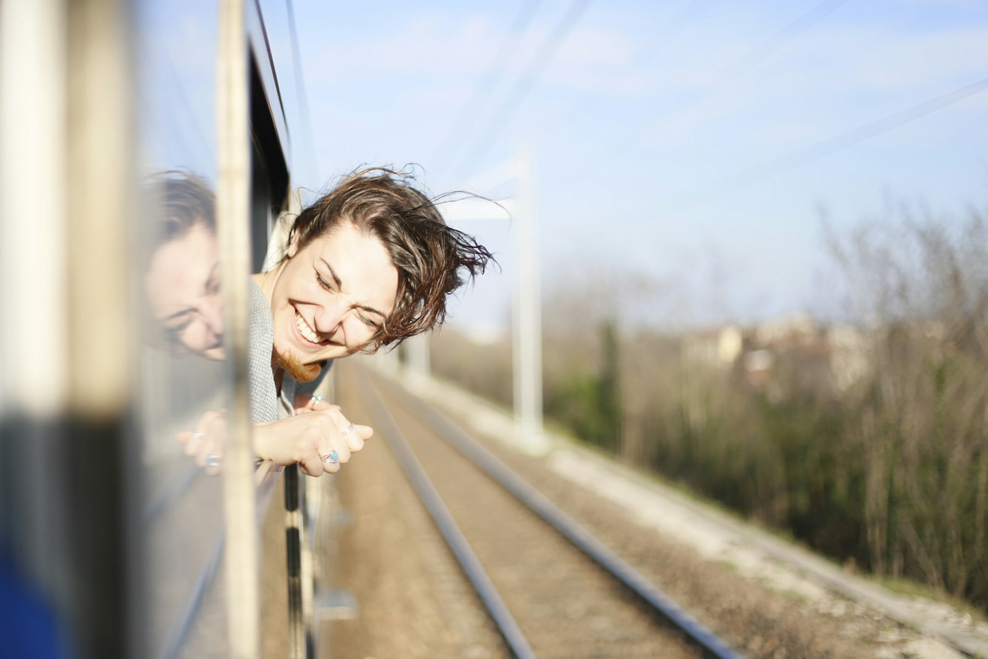 Young woman travelling on a train with her head out the window and the wind blowing her hair © Eleanor Joy Holmes / Getty Images