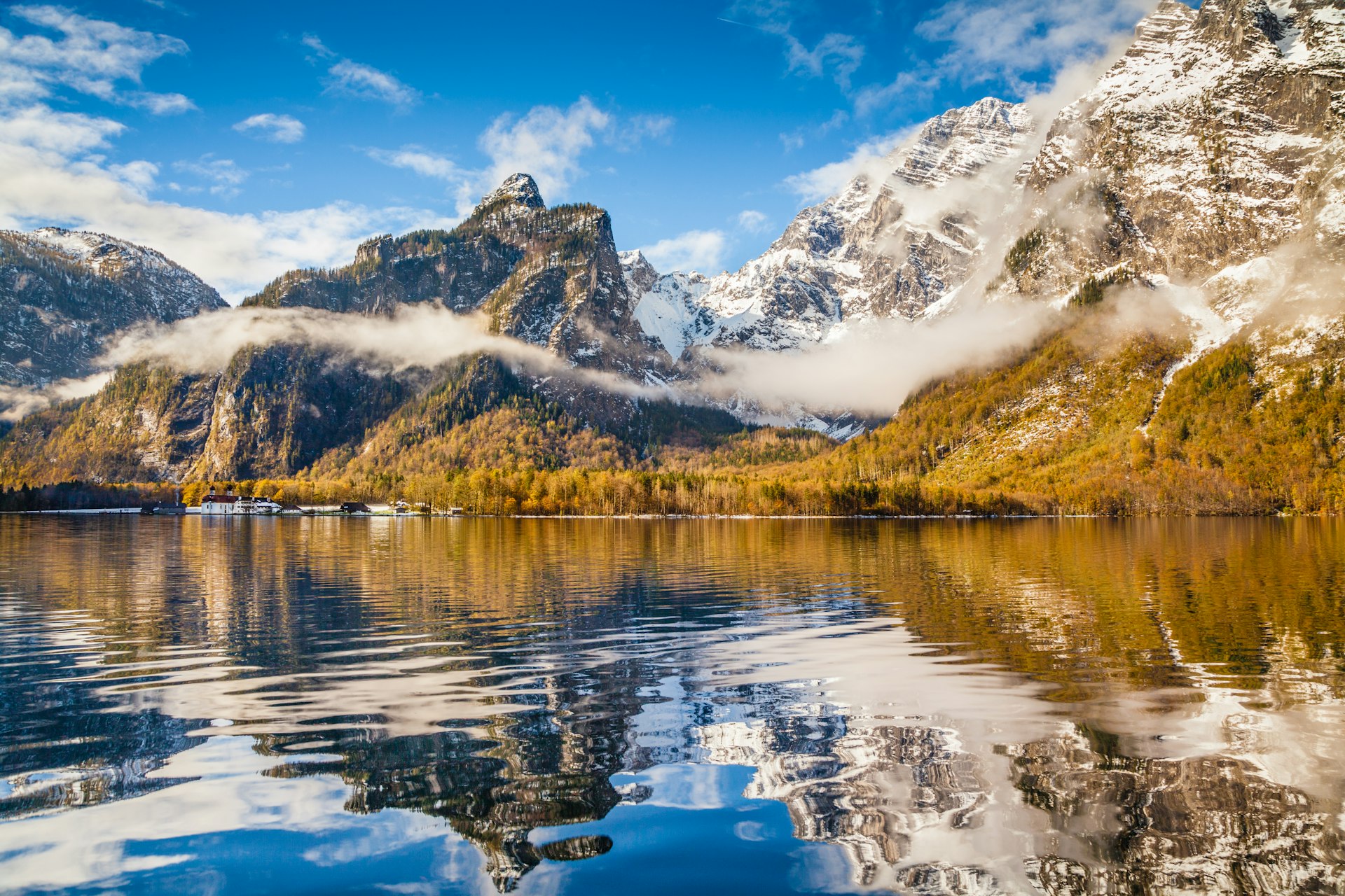 An autumn landscape of golden trees and steep snow-covered slopes wreathed in clouds next to the öԾ, Bavaria