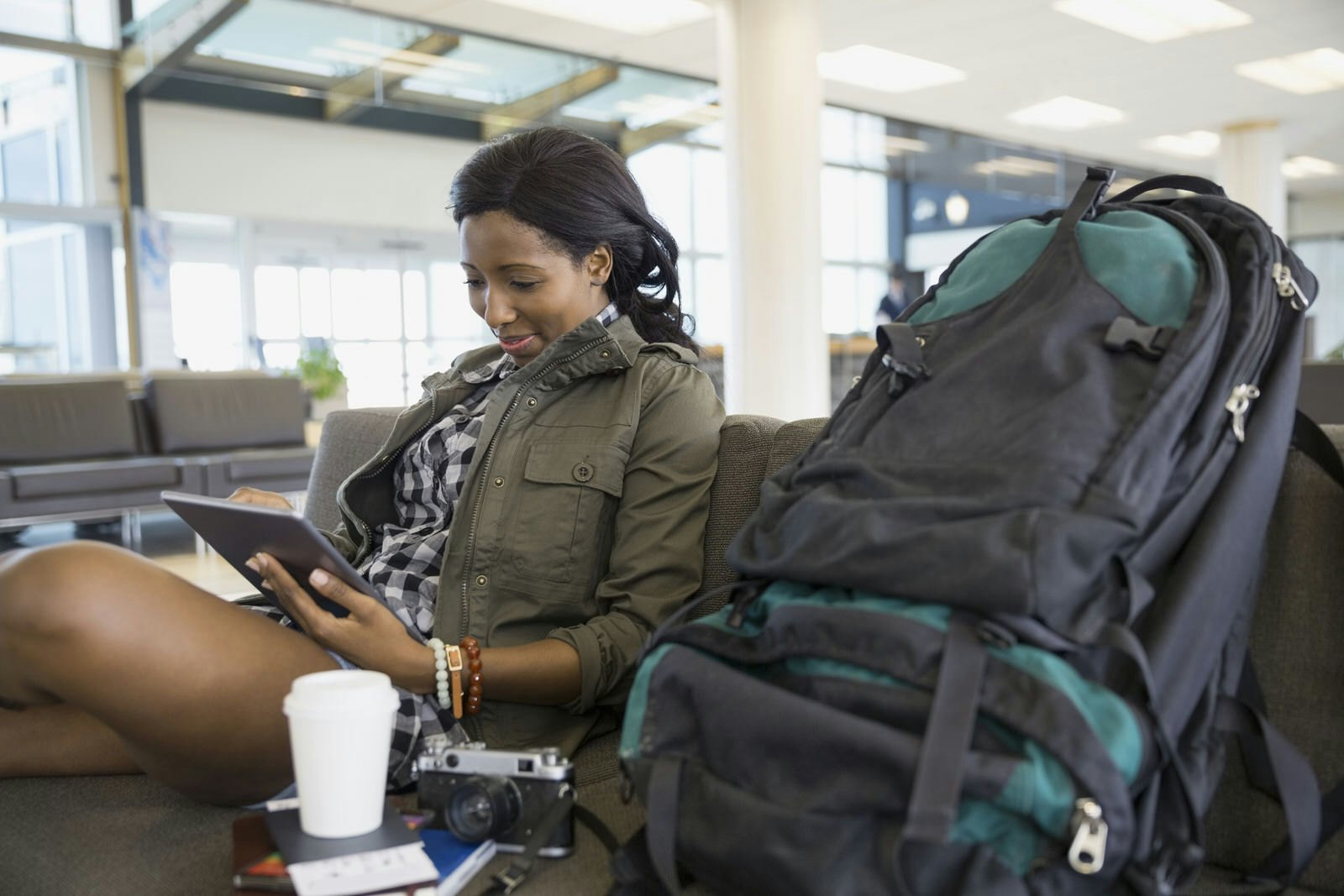 Woman sits in transport terminal browsing a tablet computer with backpack by her side © Hero Images Inc / Getty Images