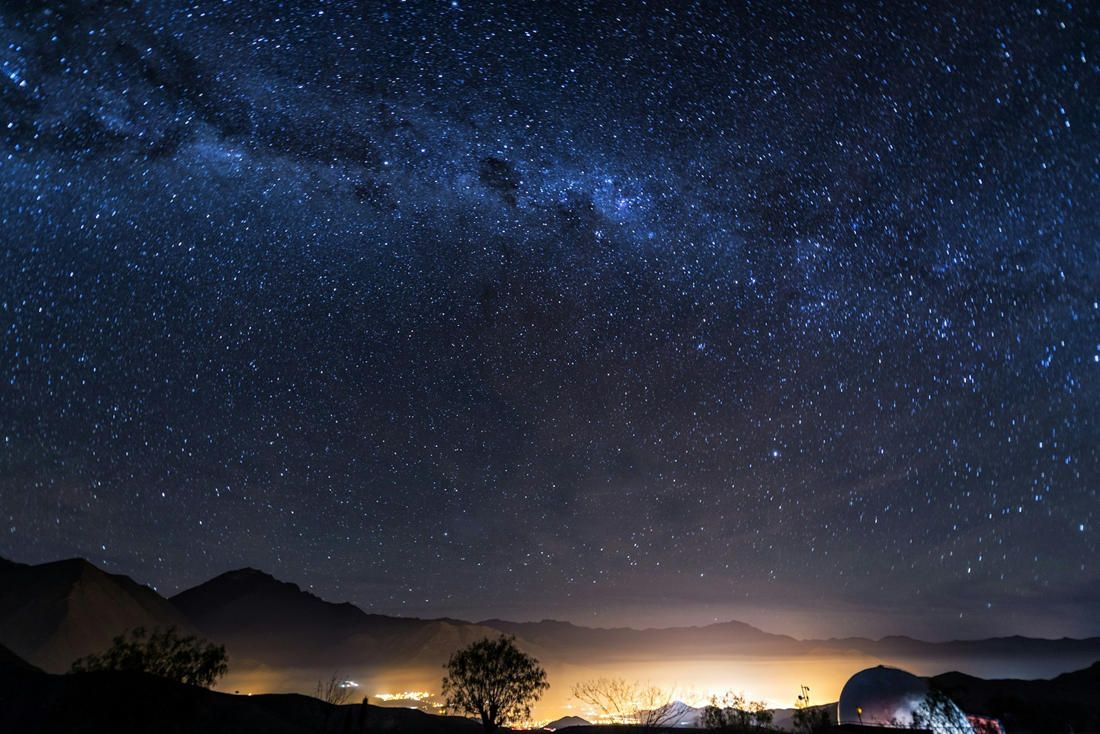 Stars of the Milky Way stretch over the Elqui Valley in Chile. Lights from a town shine below. ©DC_Colombia/Getty Images