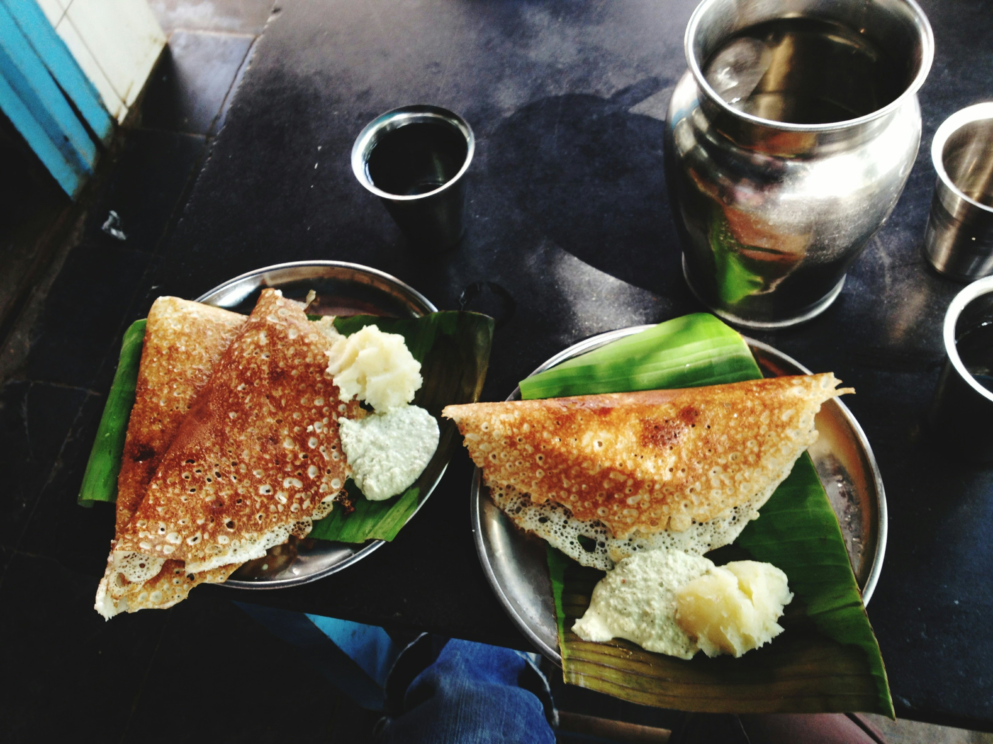 Plates with dosas and coconut chutney served on a banana leaf.