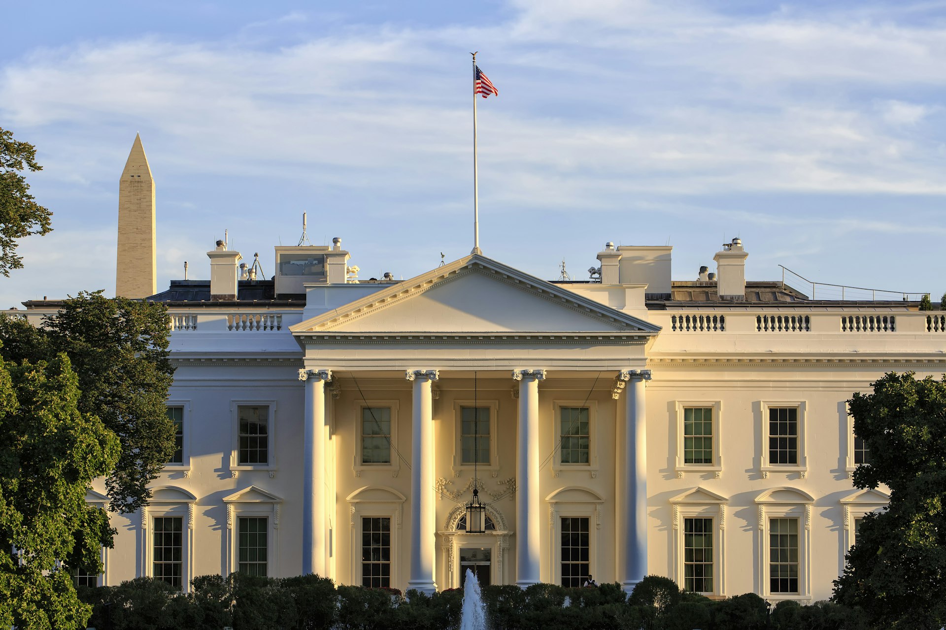 Exterior of the White House -- a large symmetrical colonnaded property with an American flag flying above it