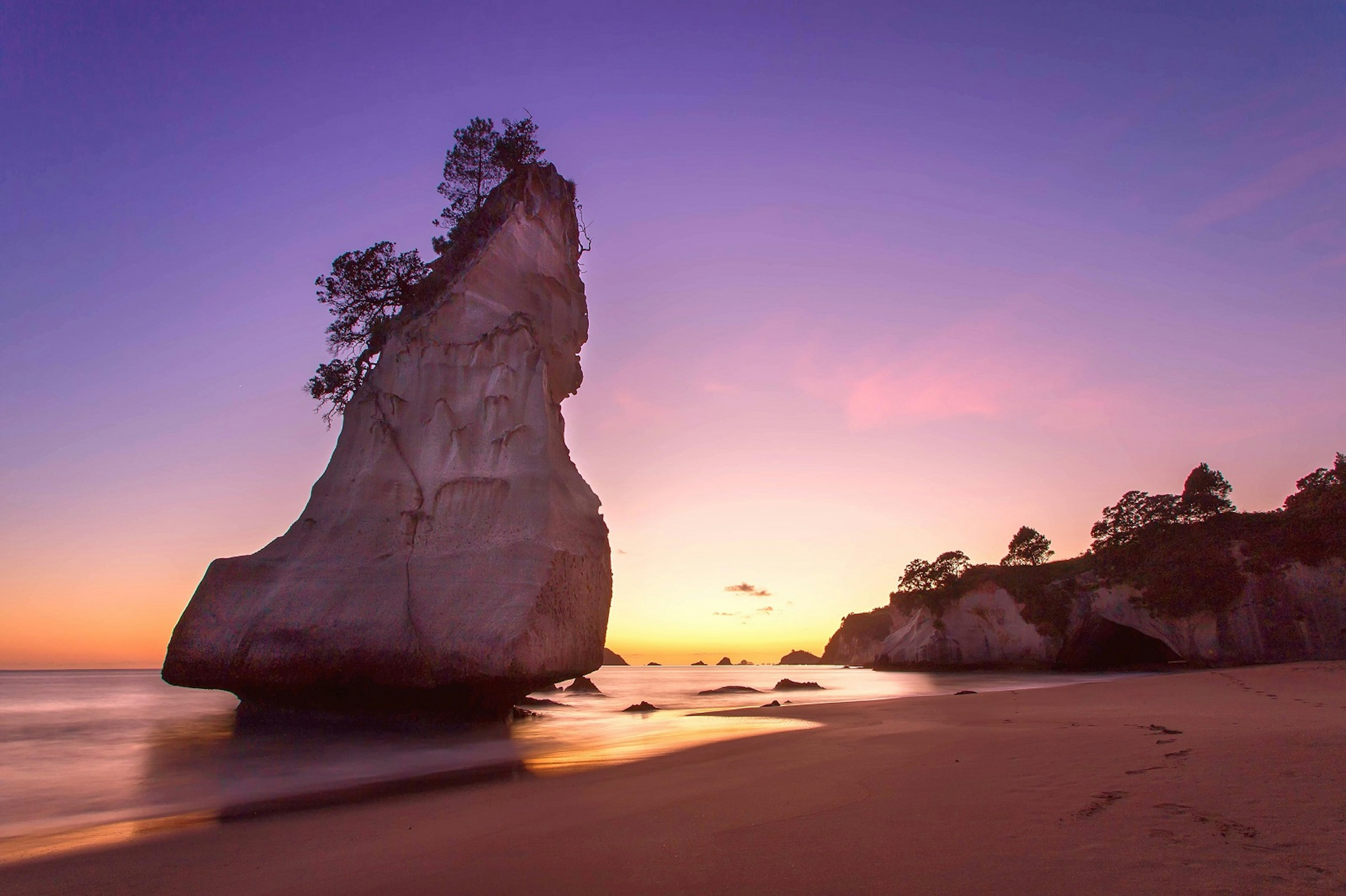 A large rock stack forms a silhouette against a sky of purples, pinks and yellows