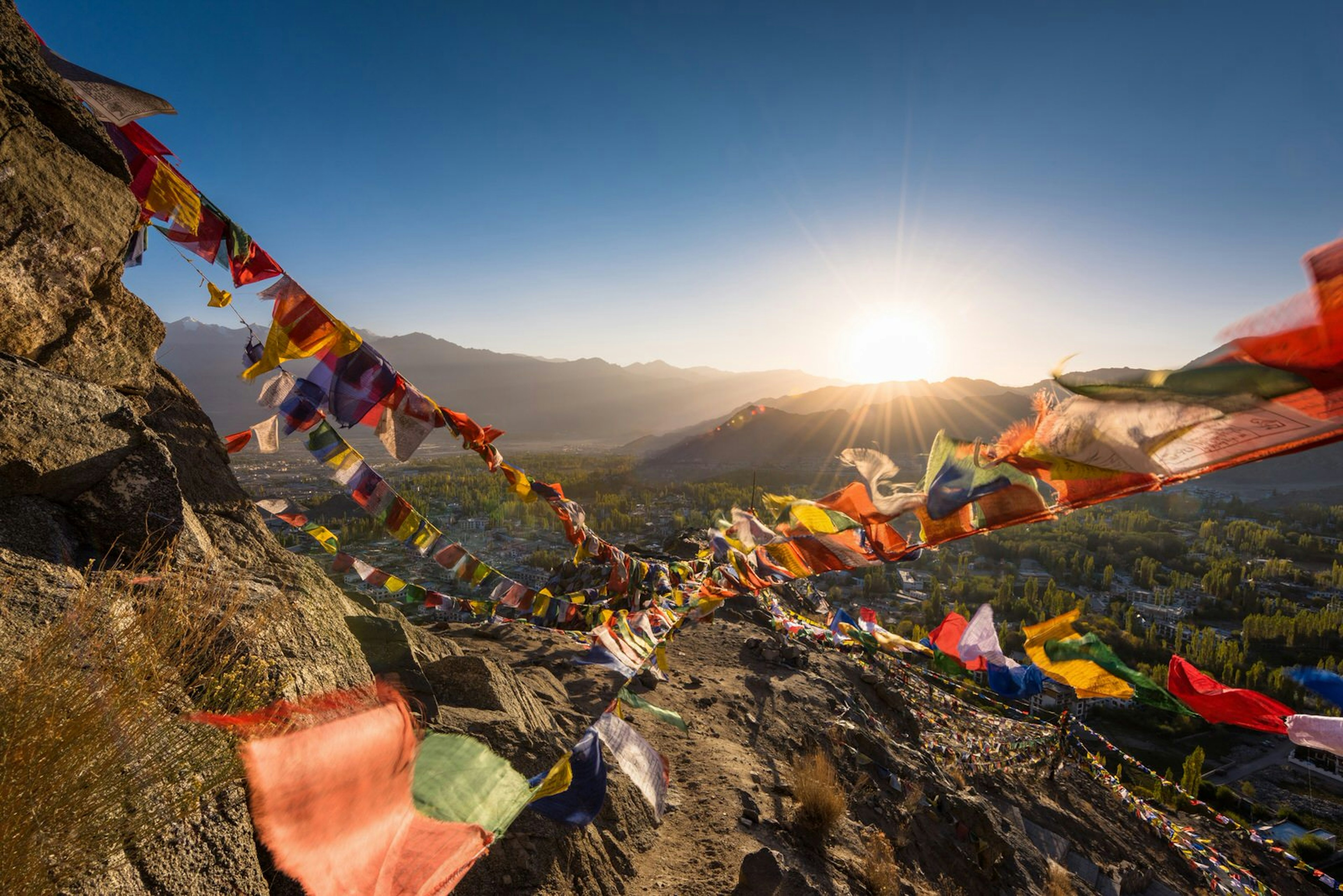 Colourful Buddhist prayer flags flutter in the breeze as the sun rises over moutains