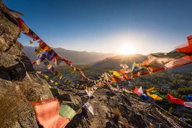 Colourful Buddhist prayer flags flutter in the breeze as the sun rises over moutains