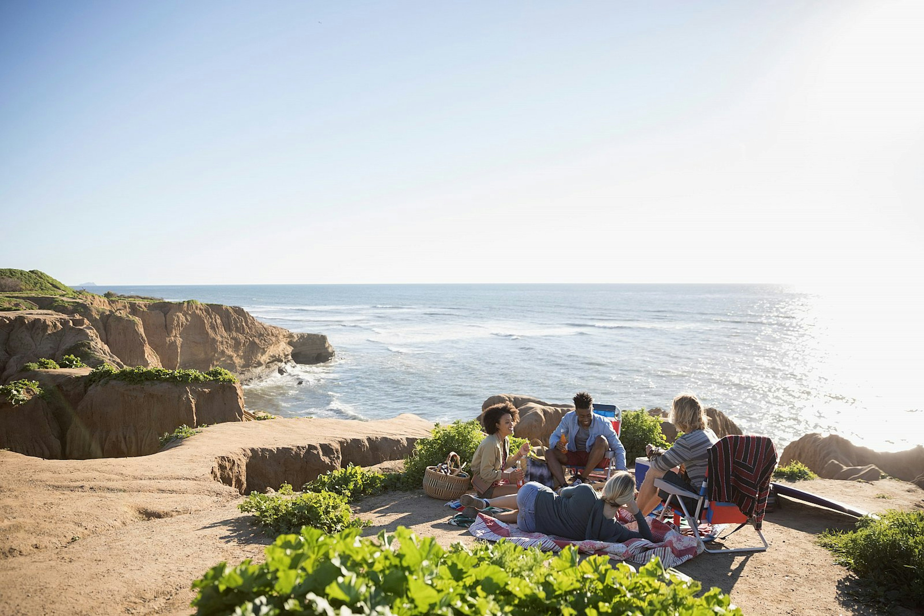 Young friends hanging out on a sunny clifftop with the ocean beyond.