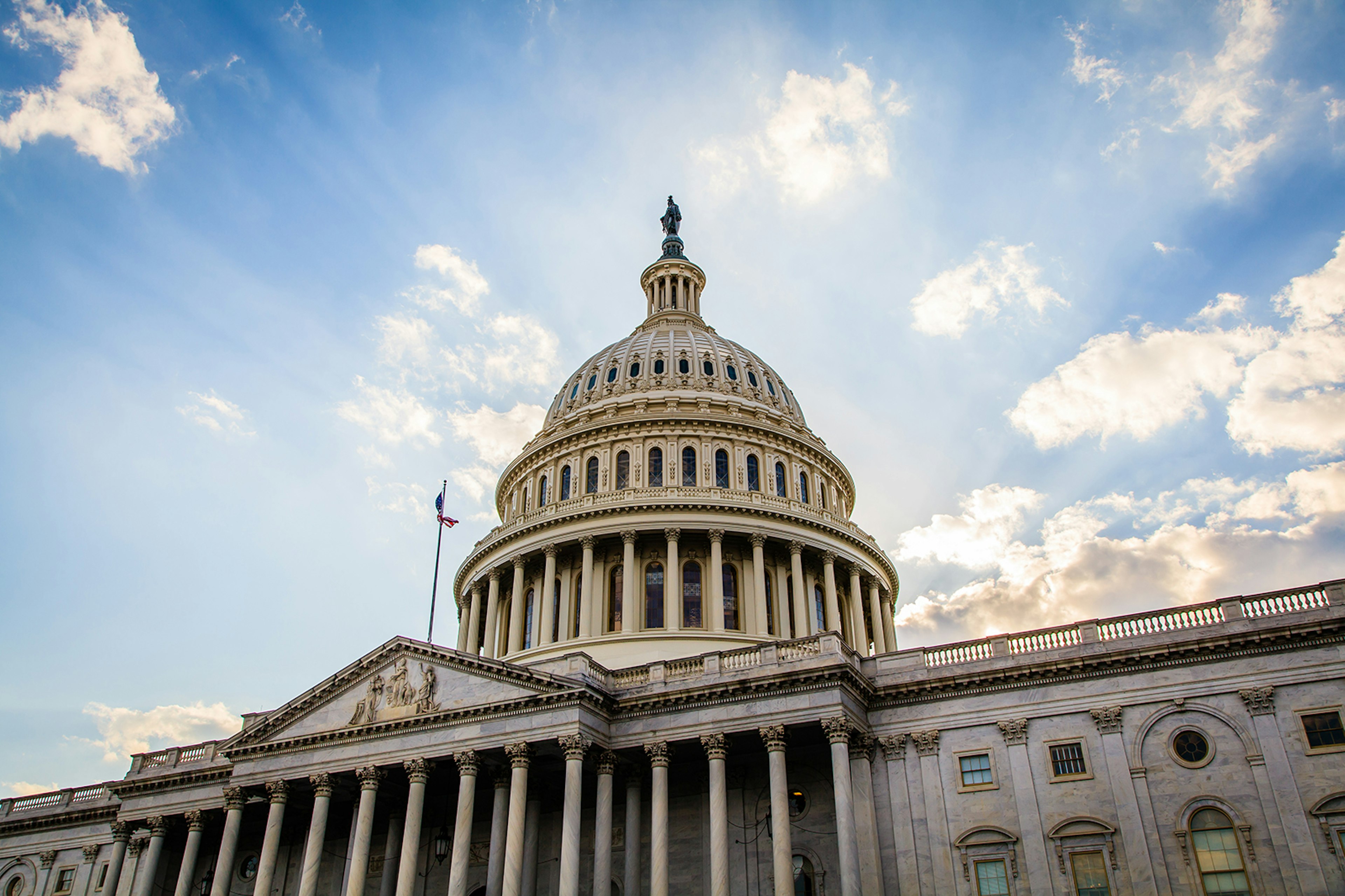 The upper dome of the US Capitol building, with rays of sunshine shining through clouds and a blue sky; Weekend in Washington, DC