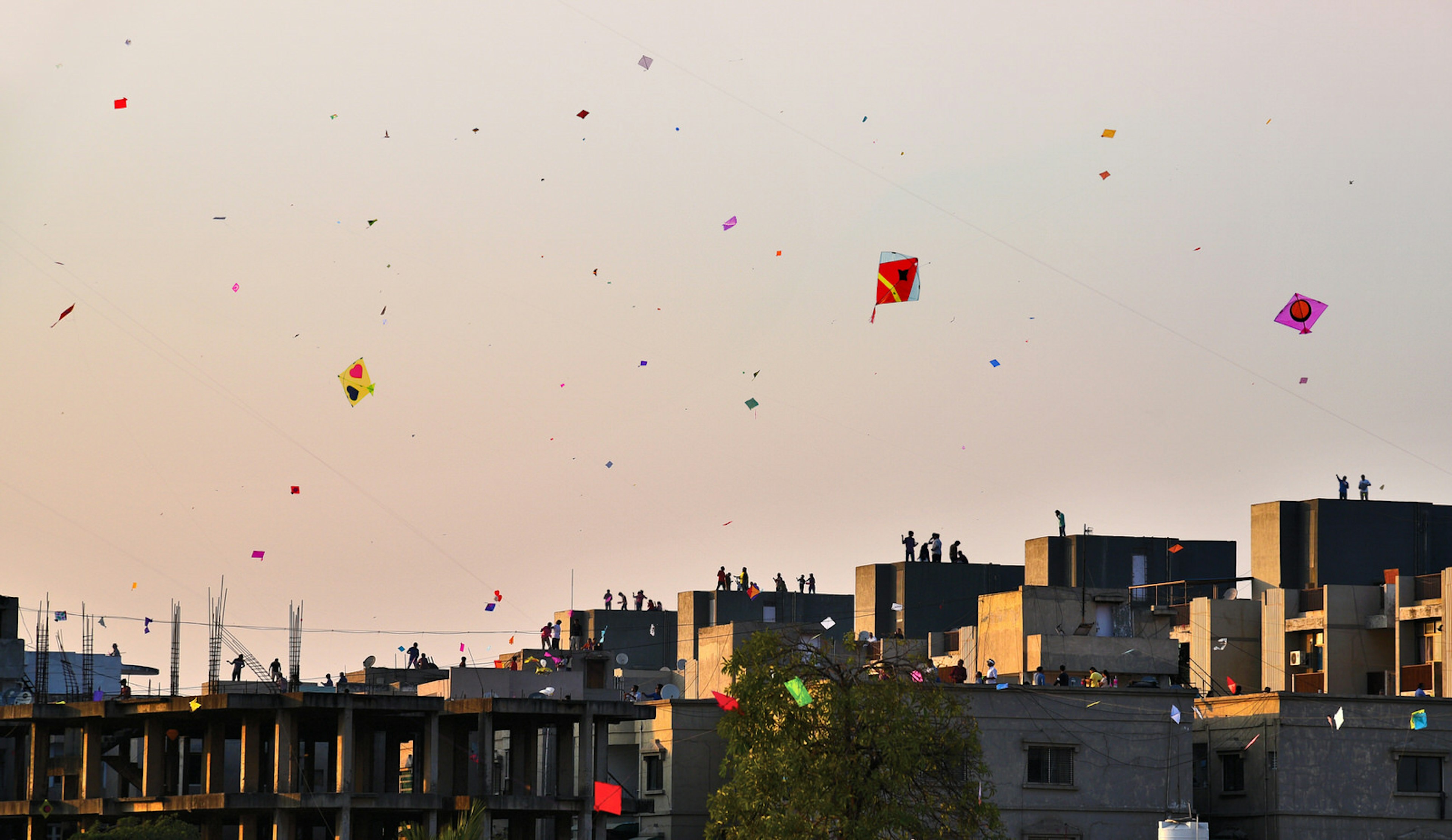 Colourful kites fly above the rooftops of Ahmedabad at dusk.