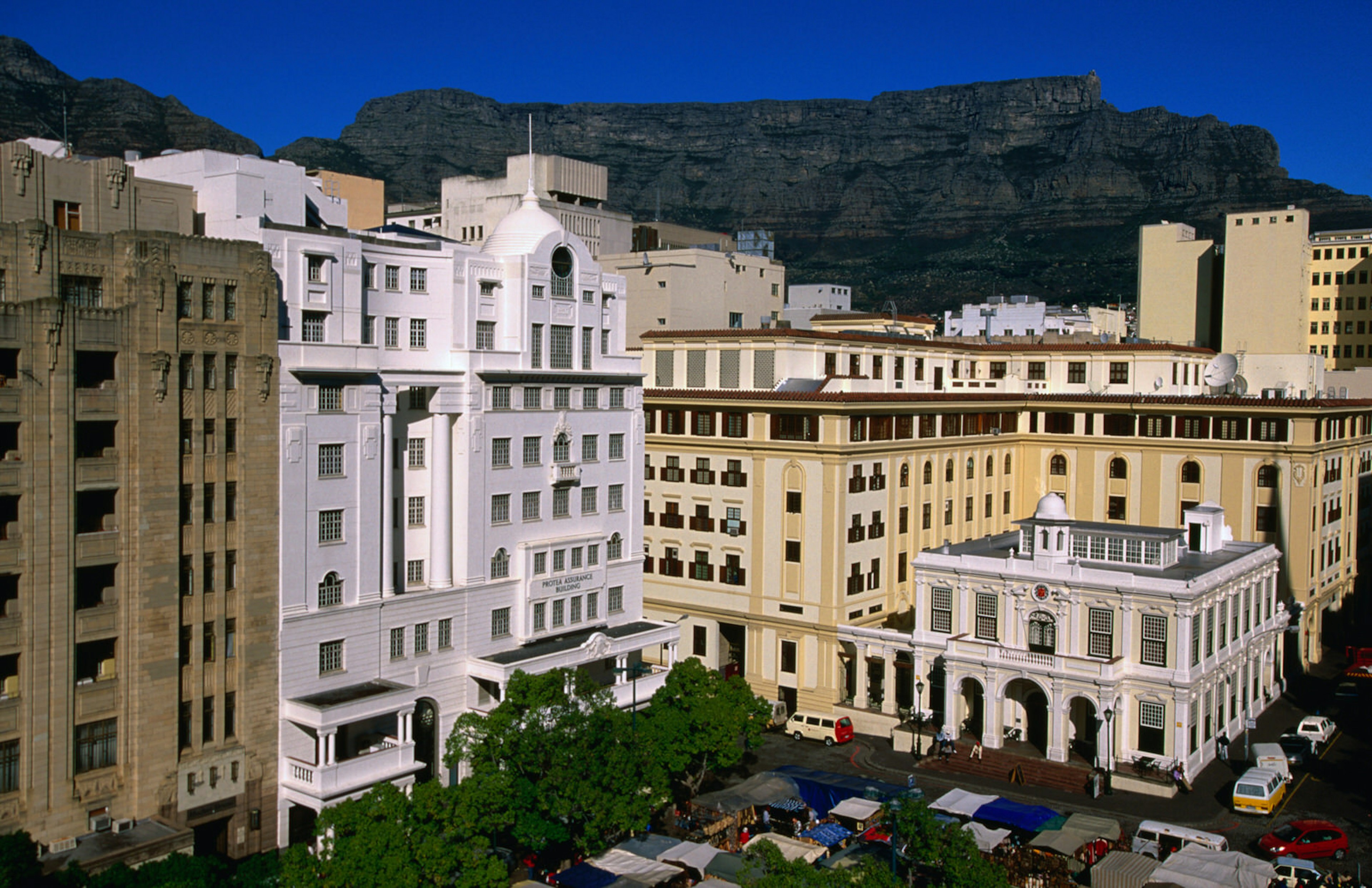 Beneath some Art Deco 10-storey buildings is the tree-filled Greenmarket Square. Between the trees are numerous stall with colourful cloth coverings © Ariadne Van Zandbergen / Lonely Planet