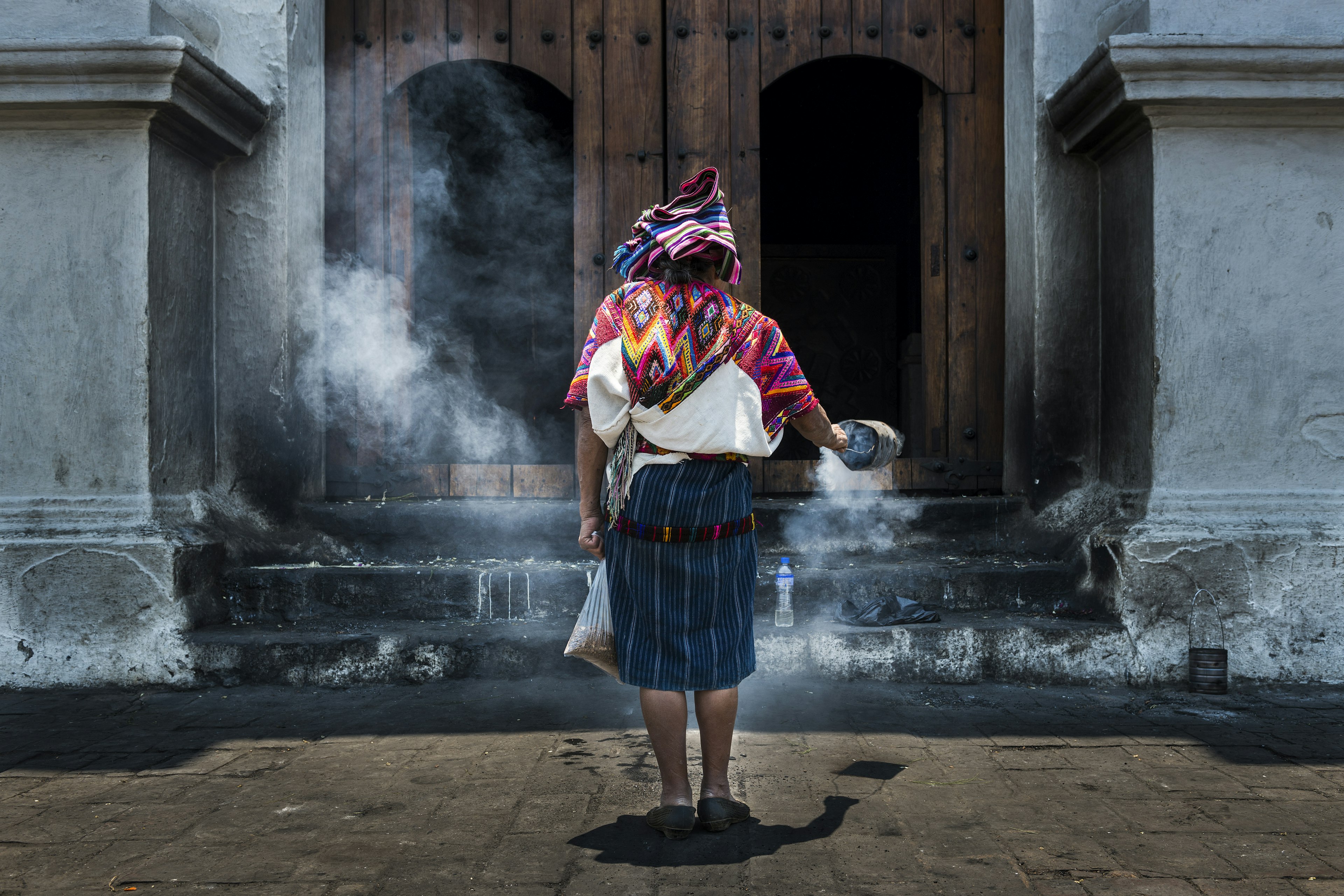 A woman dressed in a colorful Maya clothing waves a bucket filled smoke in front of Santo Tomás church in the town of Chichicastenango, in Guatemala