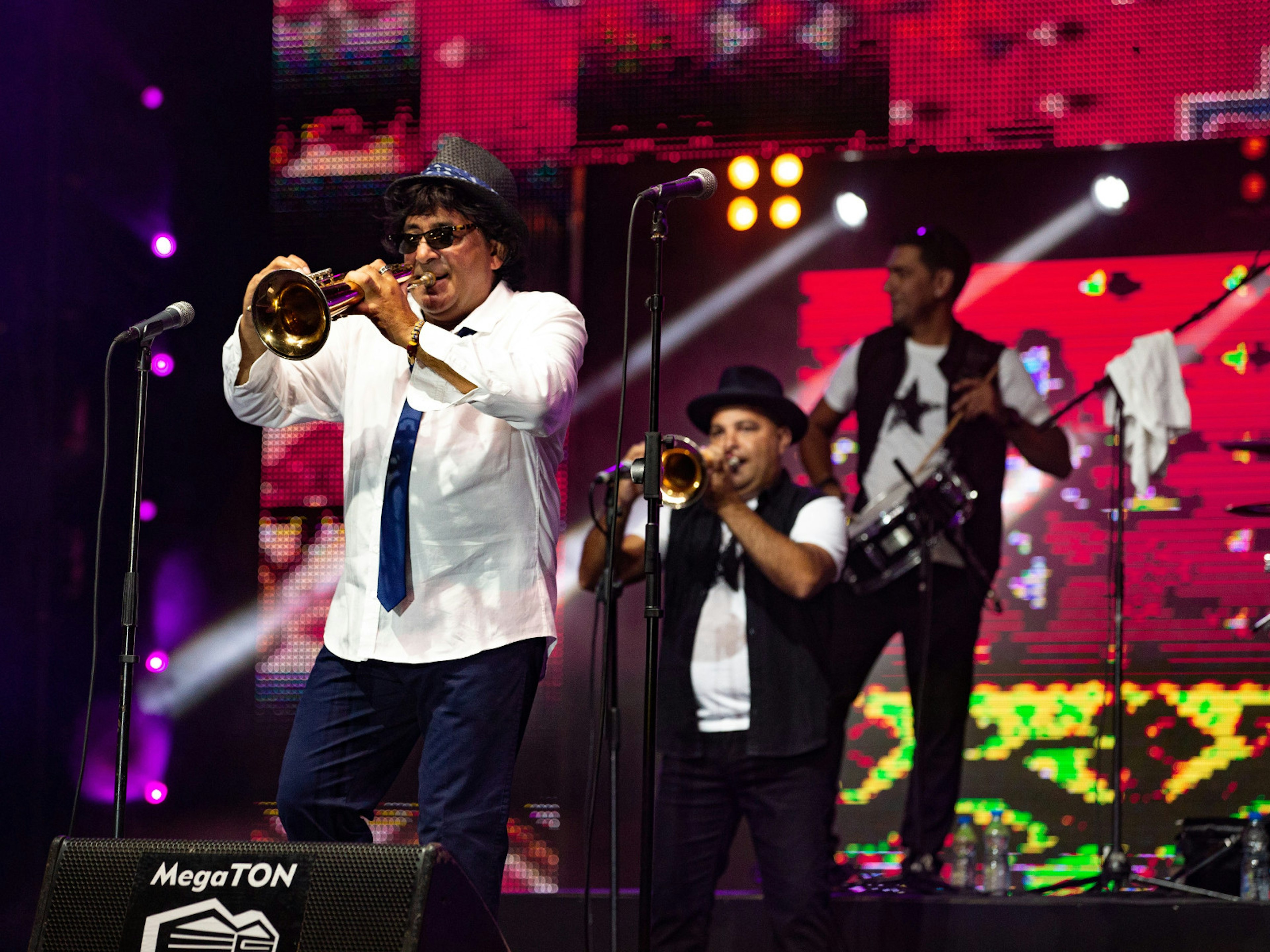 The Trumpet Master Boban Marković on stage during the 2017 festival in Guča. The stage has a large colourful screen as the backdrop and he is supported by a drummer and another trumpeter © Aleksandar Donev / Lonely Planet