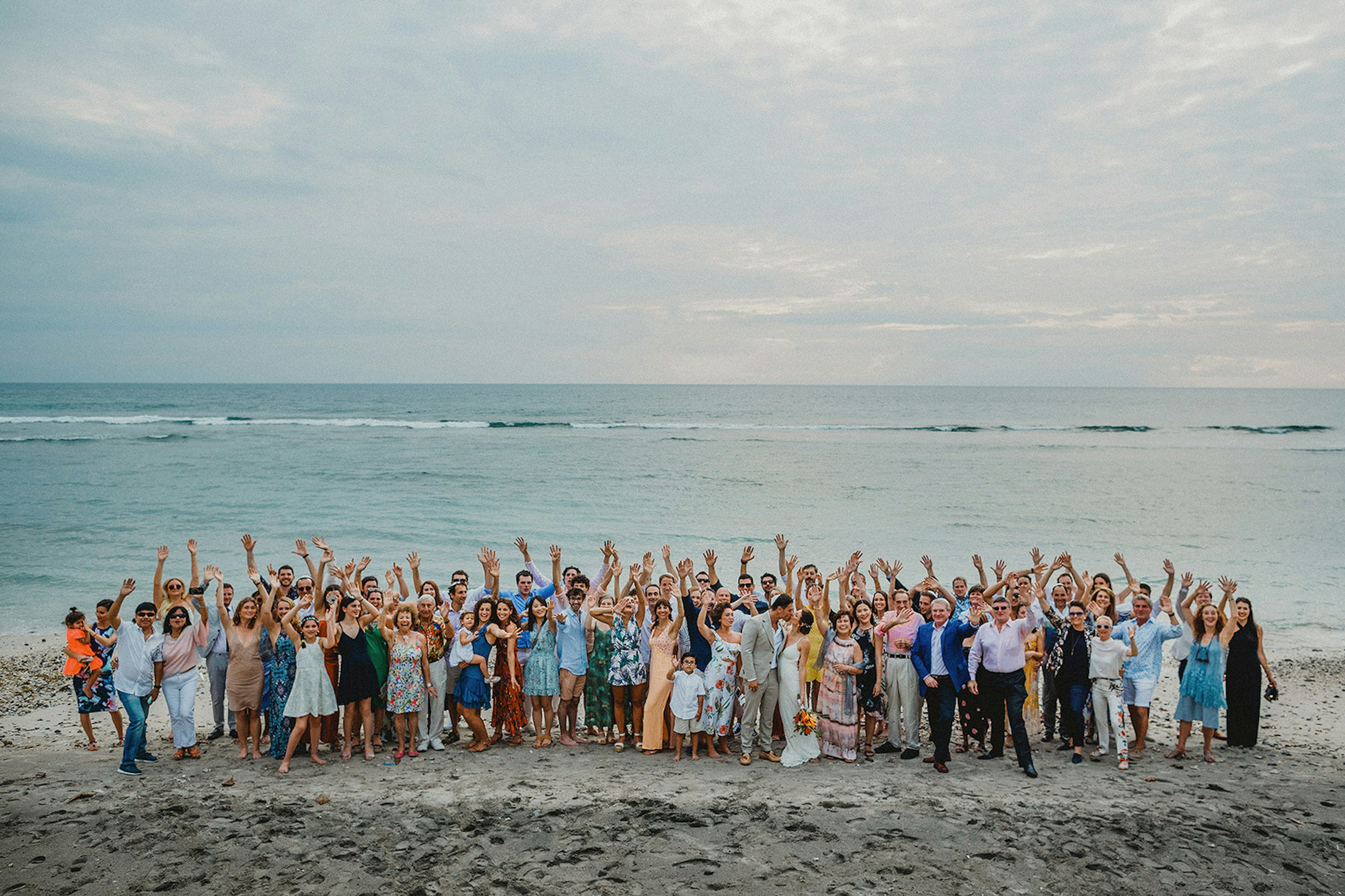 A congregation of wedding guests pose on the beach.