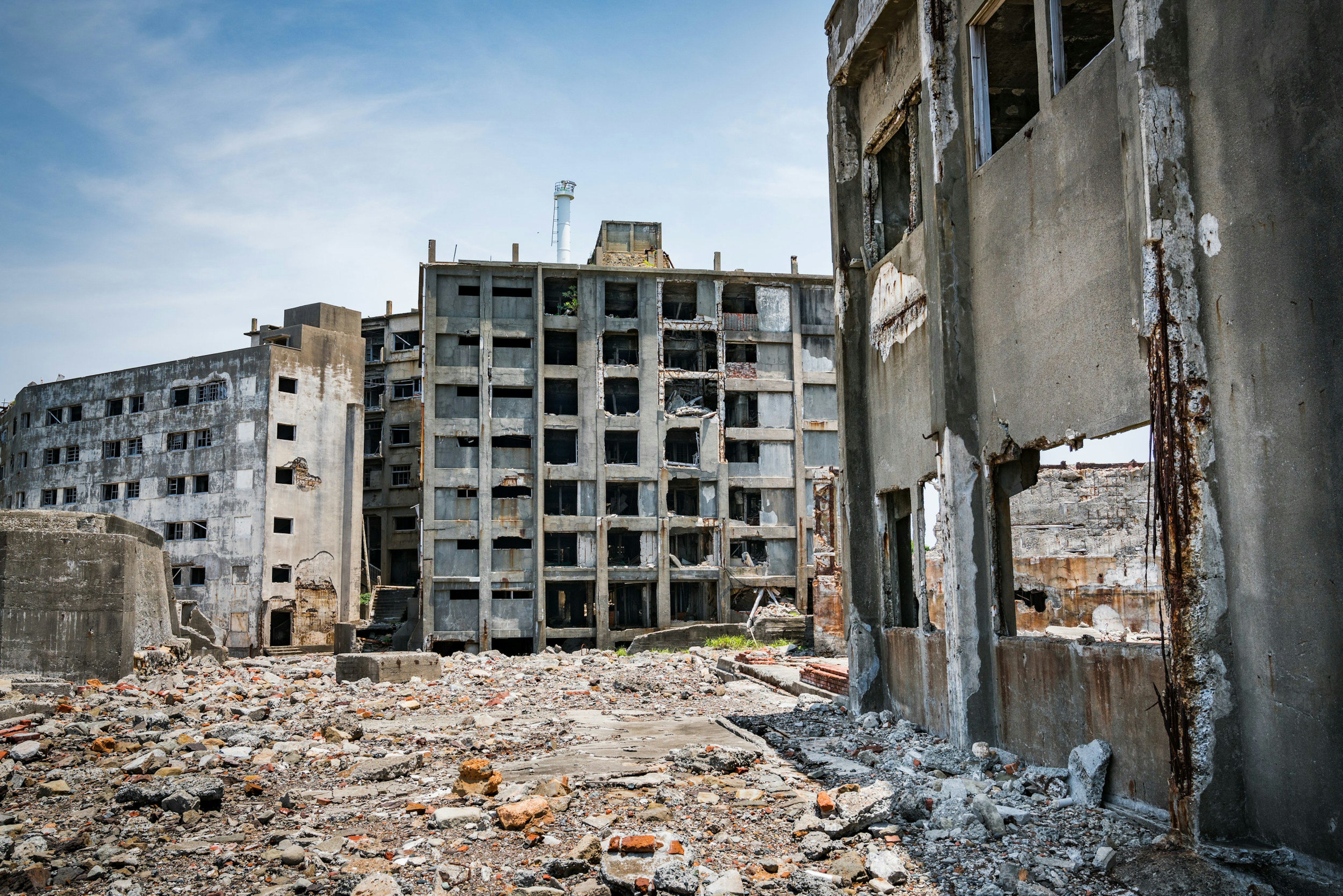 The ruins of a buildings in Hashima Island, of the coast of Japan. The ground is littered with rocks and stones.