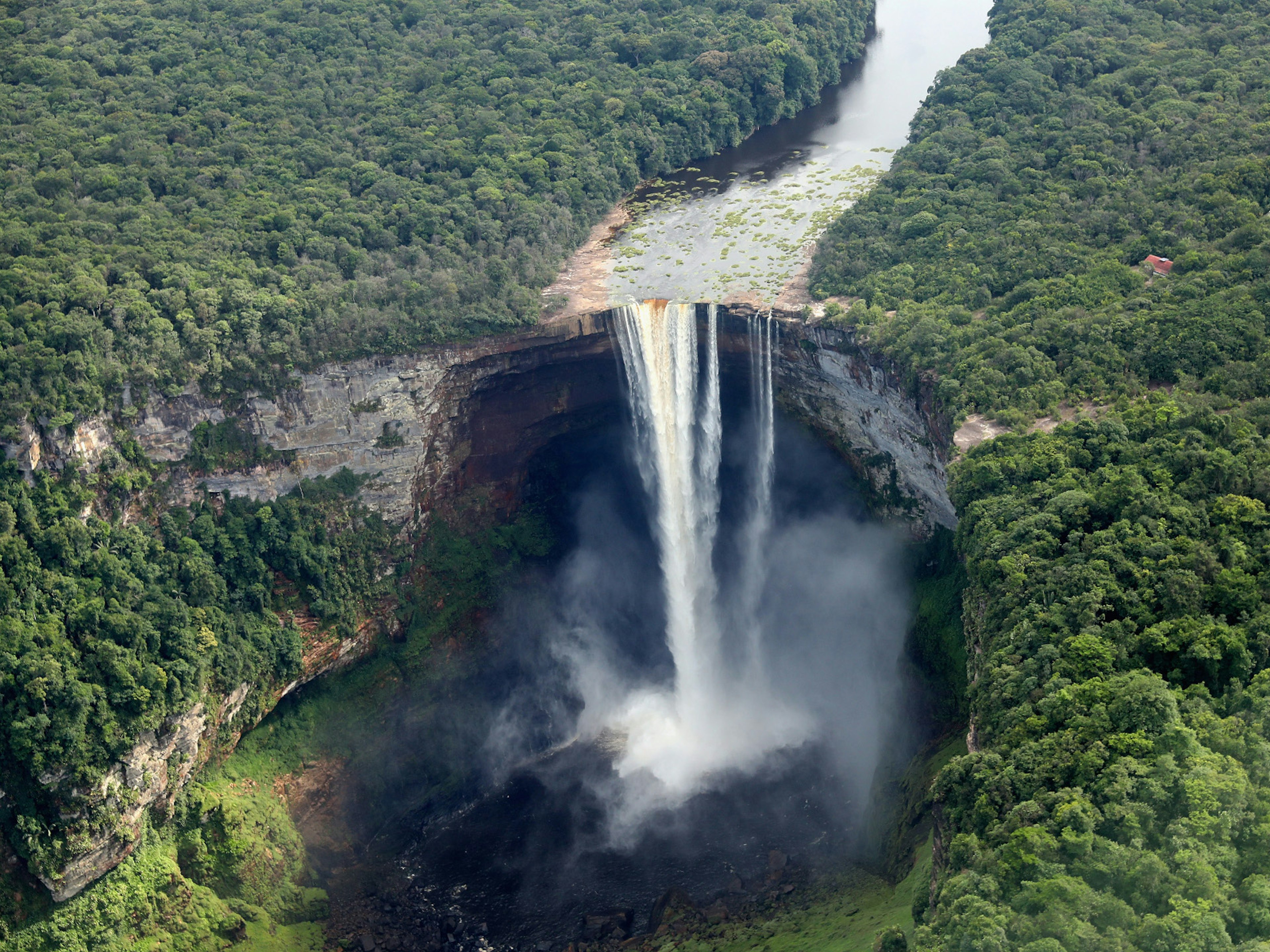 A river cutting through lush jungle gives way to a huge curved hole, which the water thunders through