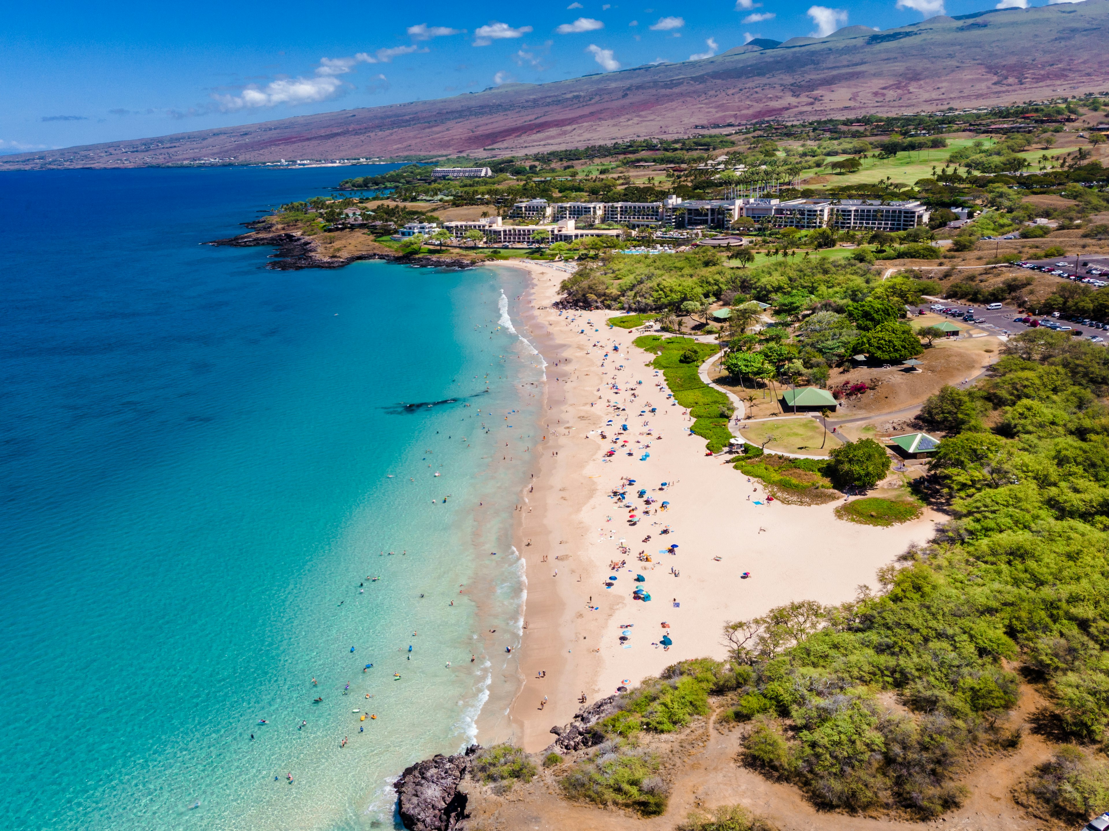 Looking down on a white sand beach dotted with sunbathers at the edge of a beautiful blue ocean