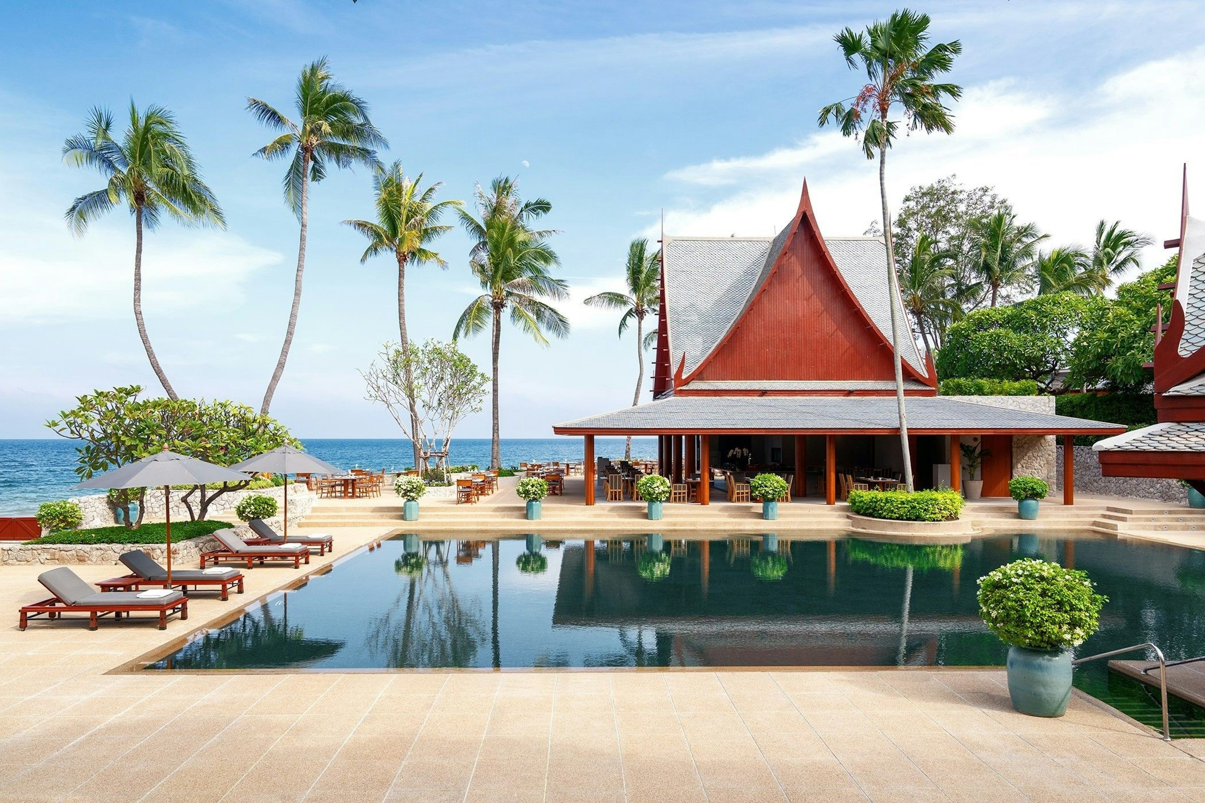 Deck chairs under umbrellas are next to an outdoor pool in Thailand