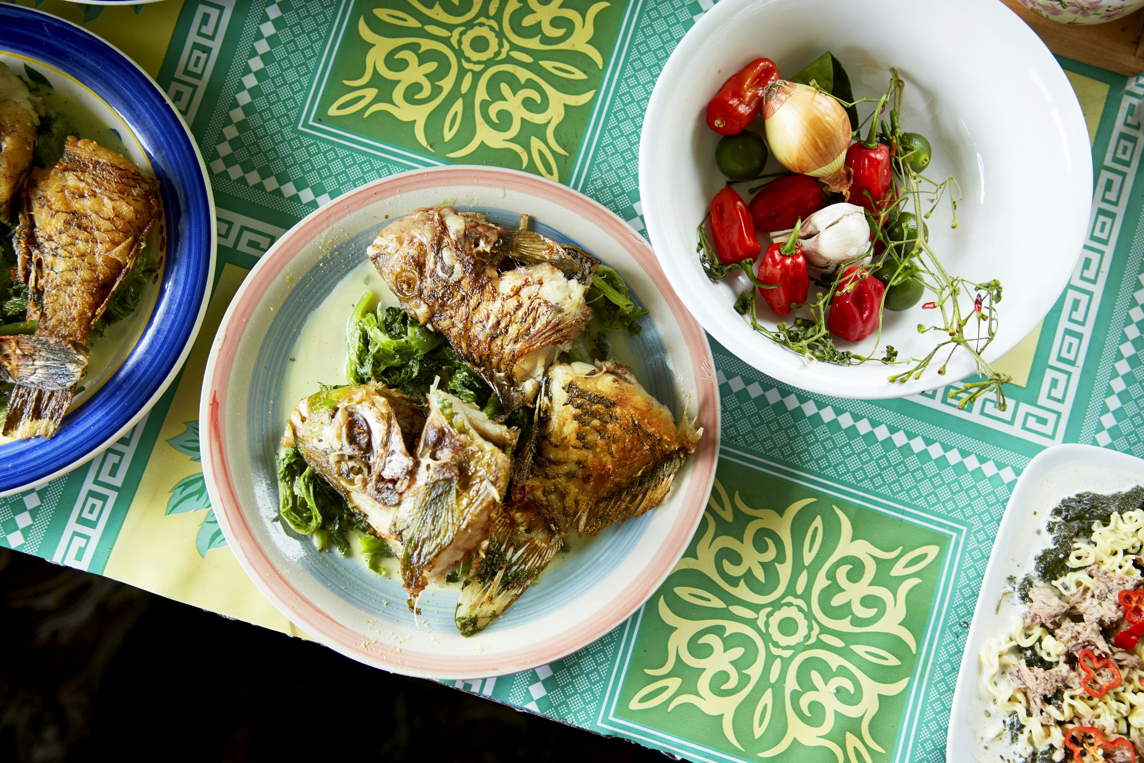 A top-down view of a table containing a number of dishes from Fiji. Most of the dishes consist of fish and fresh vegetables.