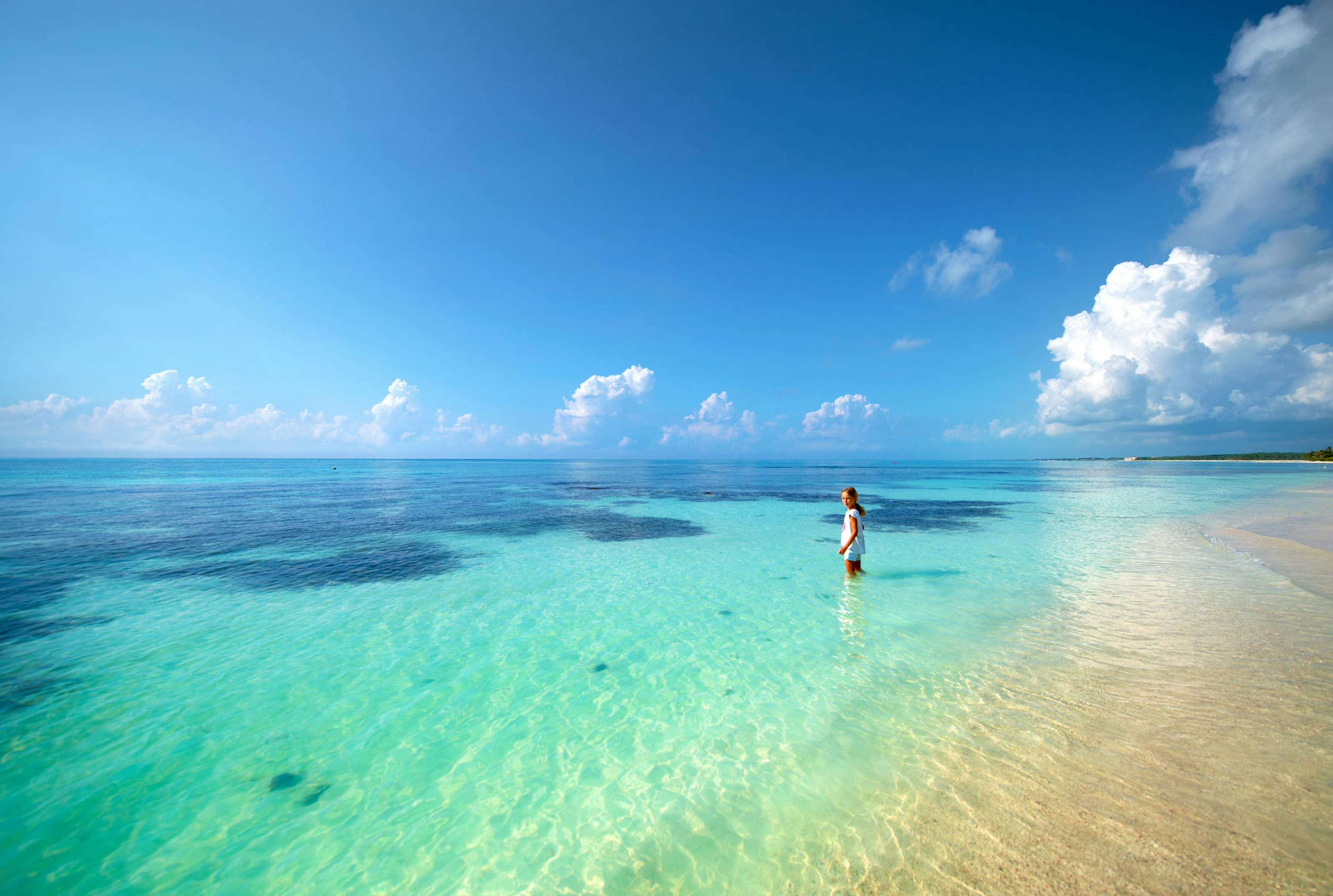 A girl stands in the shallow water of a turquoise ocean