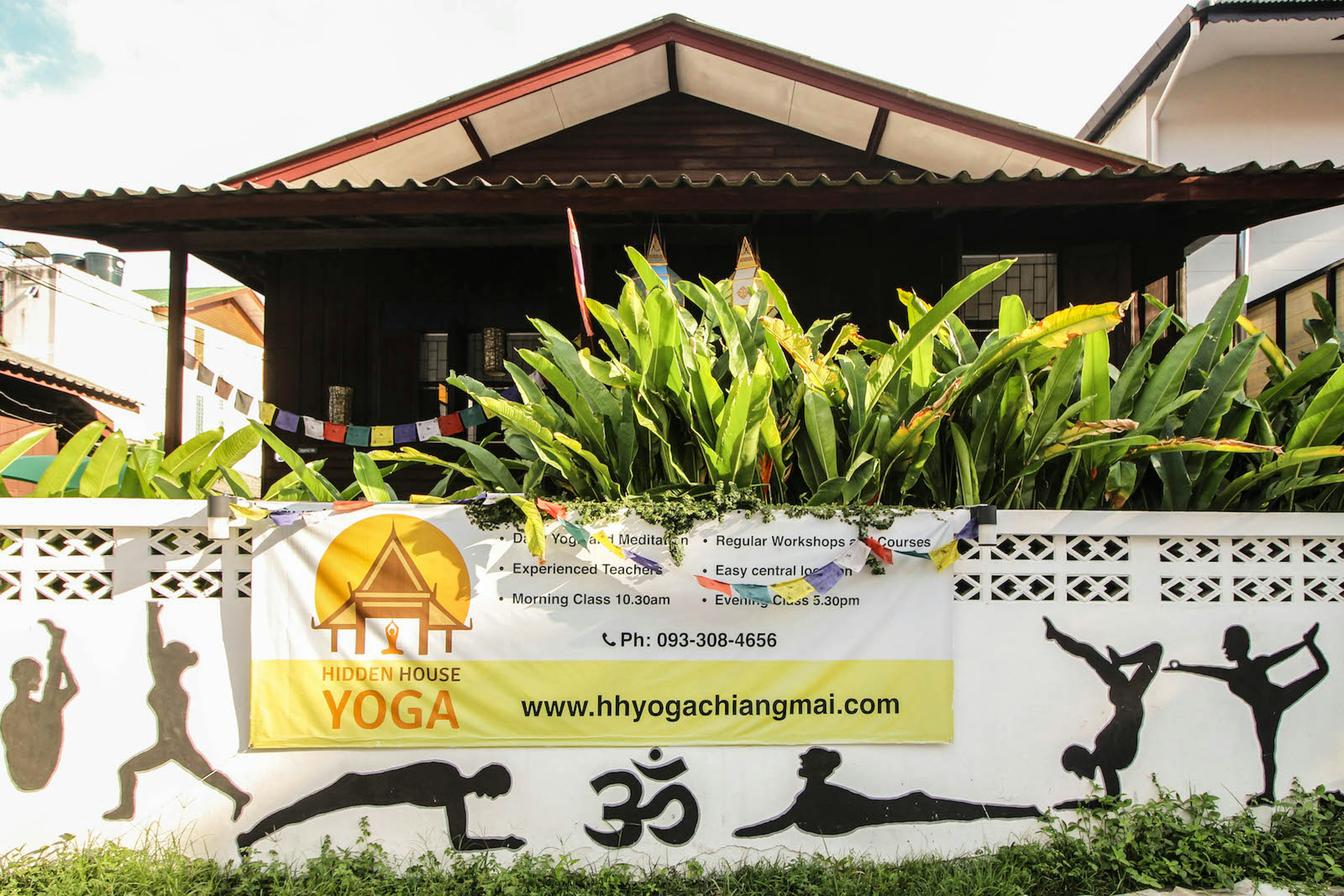 A house behind foliage surrounded by a fence with painted yoga silhouettes