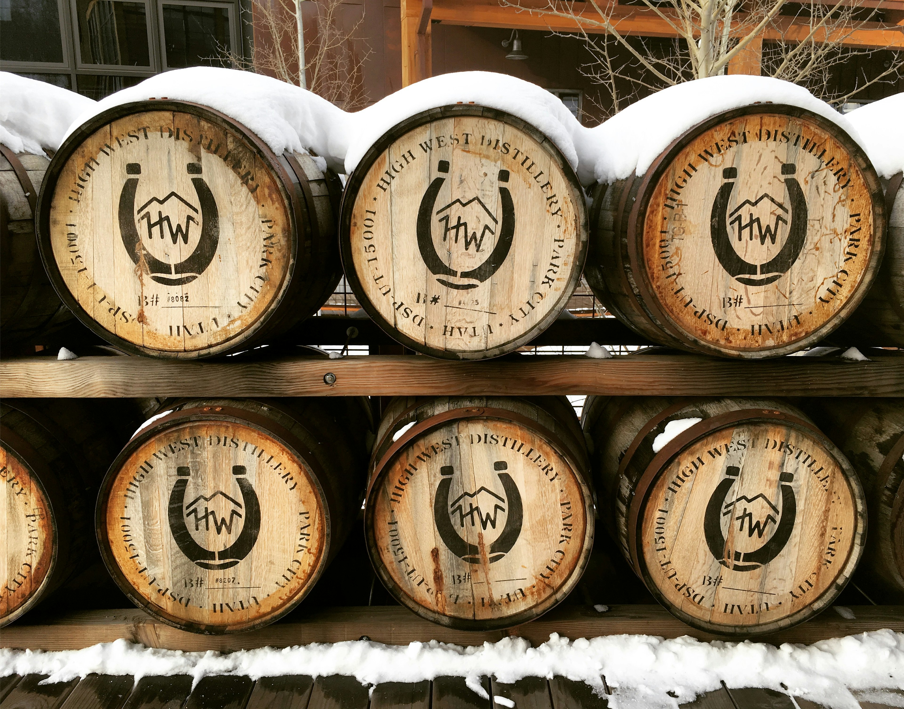 Two rows of wooden barrels are shelved outside. The barrels on the top are covered with snow; unusual distilleries