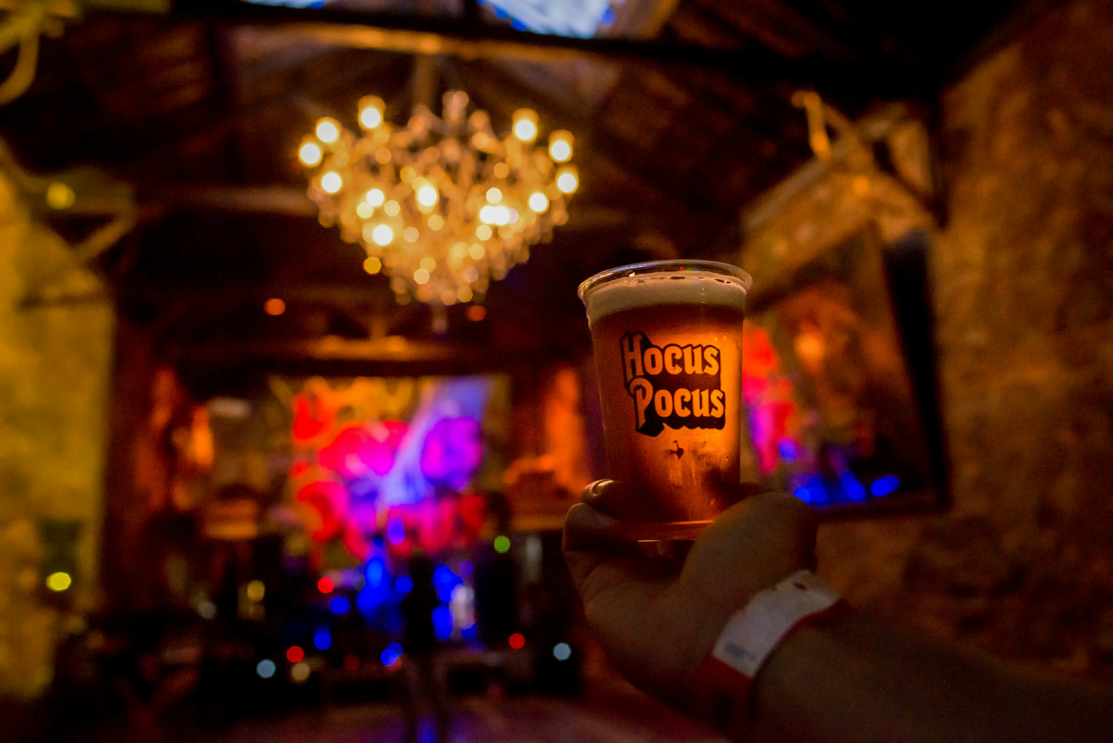 A man holds up a beer cup with the words Hocus Pocus in an atmospheric music venue with a large chandelier in Rio de Janiero, Brazil