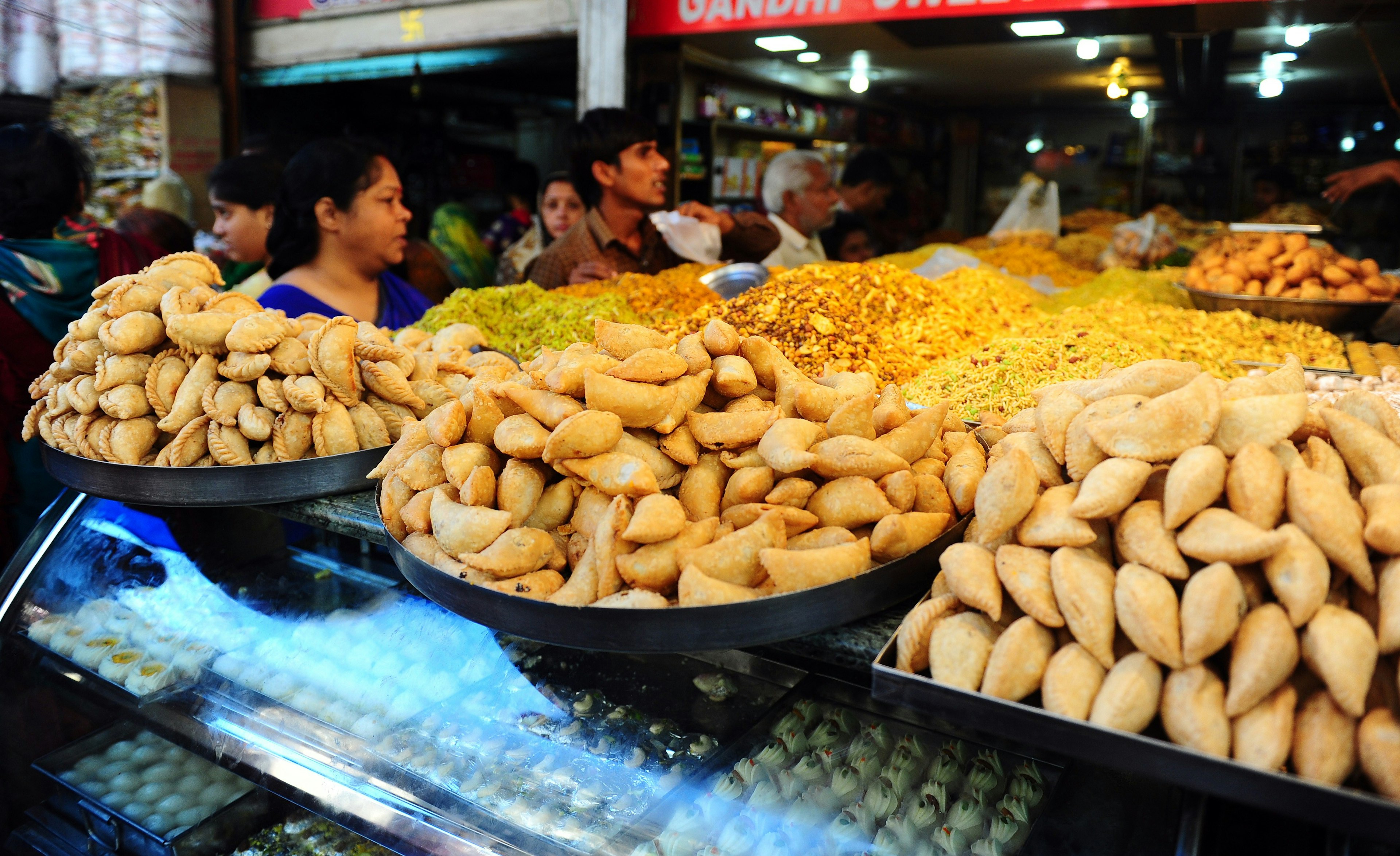 Locals purchase traditional sweets for Holi celebrations at a roadside stall in the old city in Allahabad. The countrtop is full of foods of different shapes and sizes, including bowls of gujiya, a small, sweet pastry.