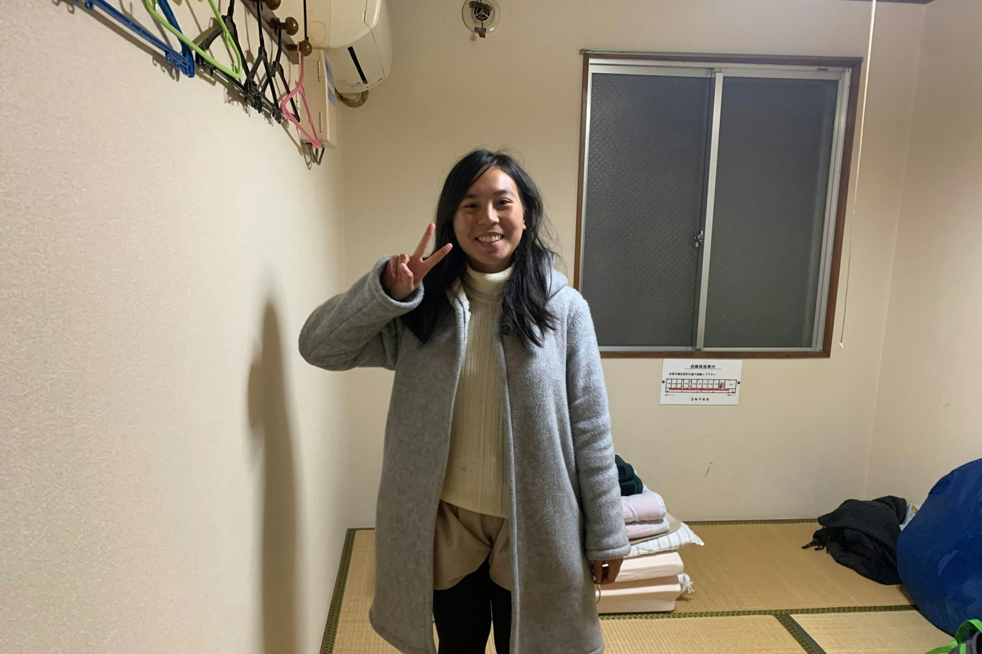 An Asian woman in a bedroom givinbg the peace sign to the camera