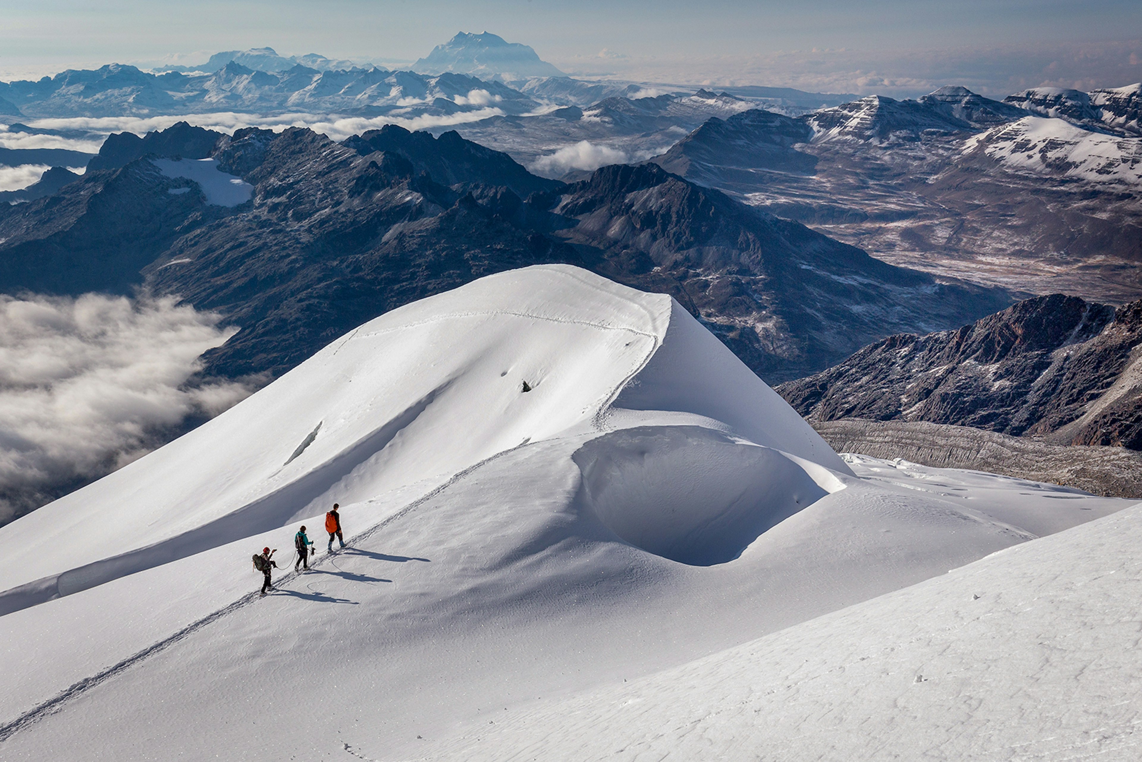 Three trekkers walk across a snowy slope with a rocky mountain range in the background © Subbotsky / Getty Images