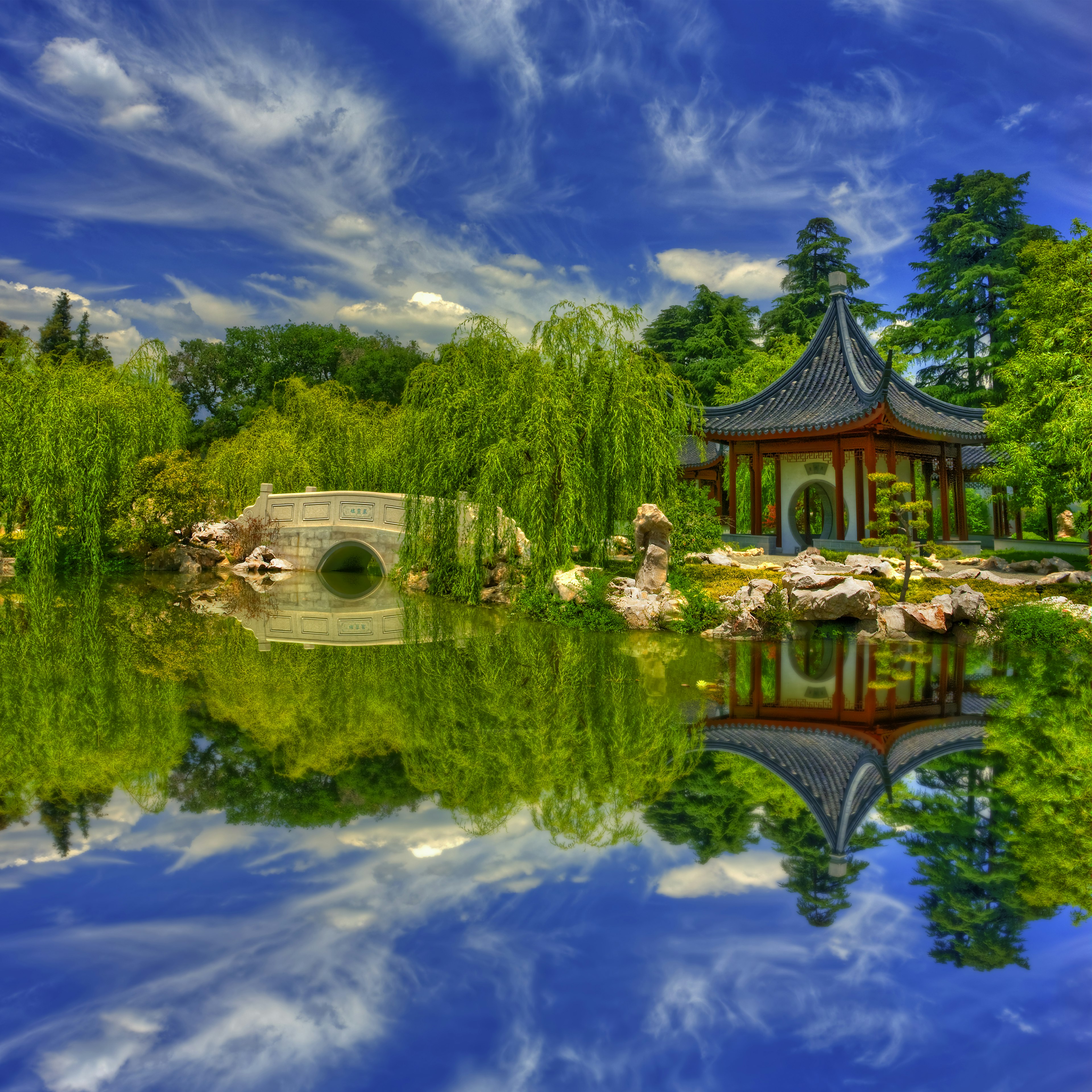 A white bridge blanketed by willow trees near a pristine lake. There is a red pagoda replica on the other end of the Huntington Library, Art Collections & Botanical Gardens