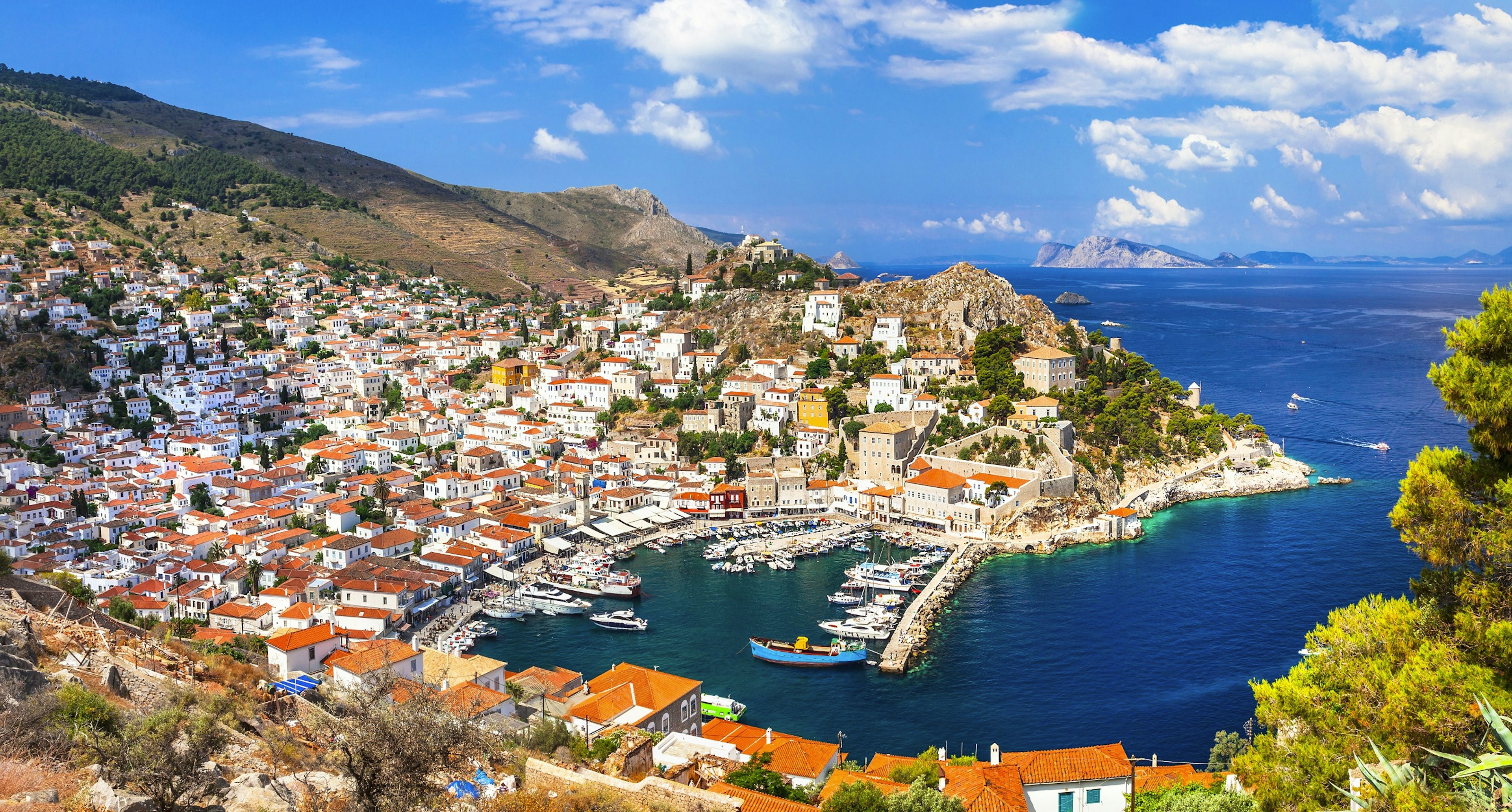 A town of white buildings with orange-red roofs, built around a curved bay with a harbour full of small fishing boats.