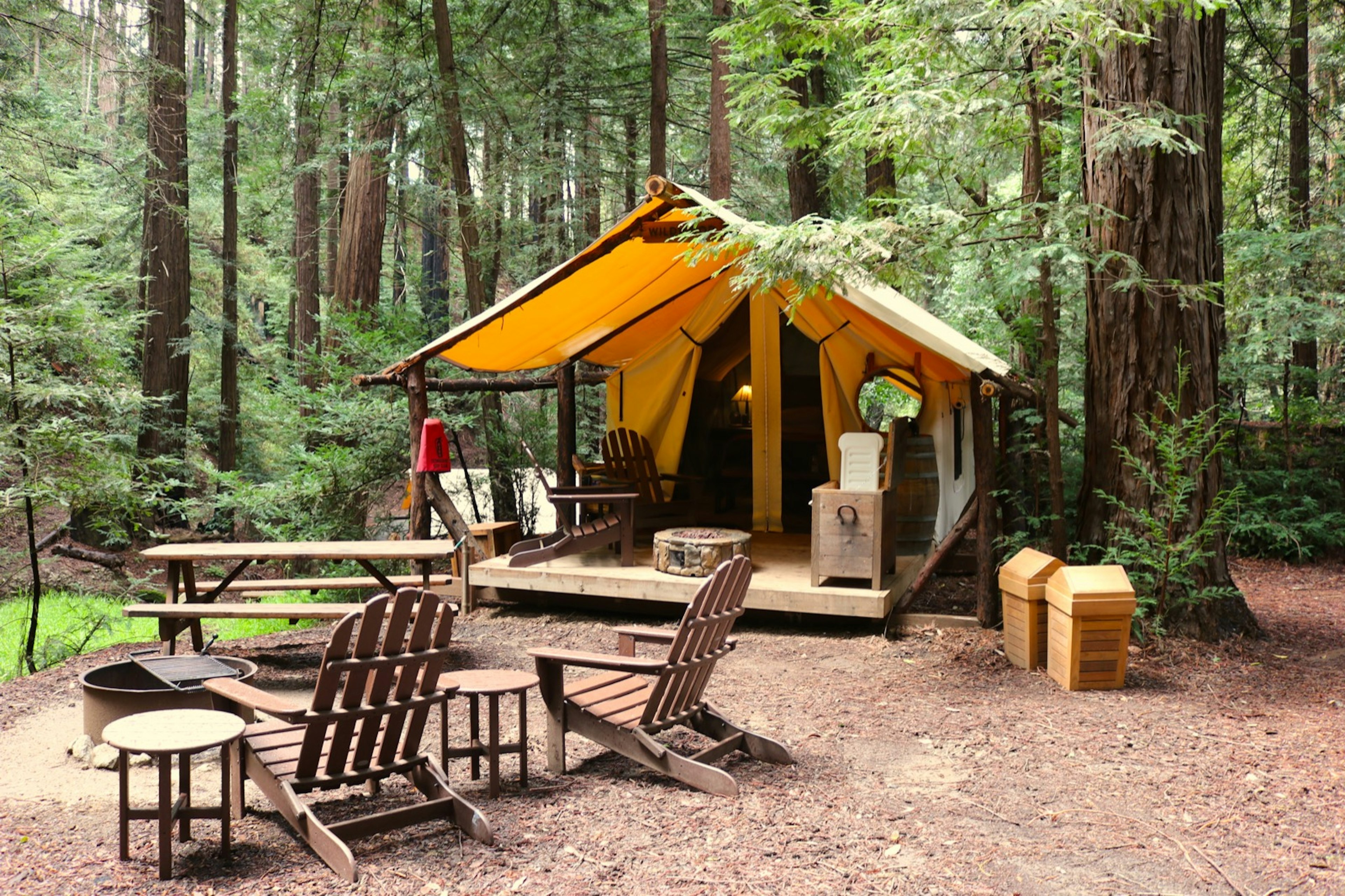 Adirondack chairs surround a fire pit with a safari-style tent in the background