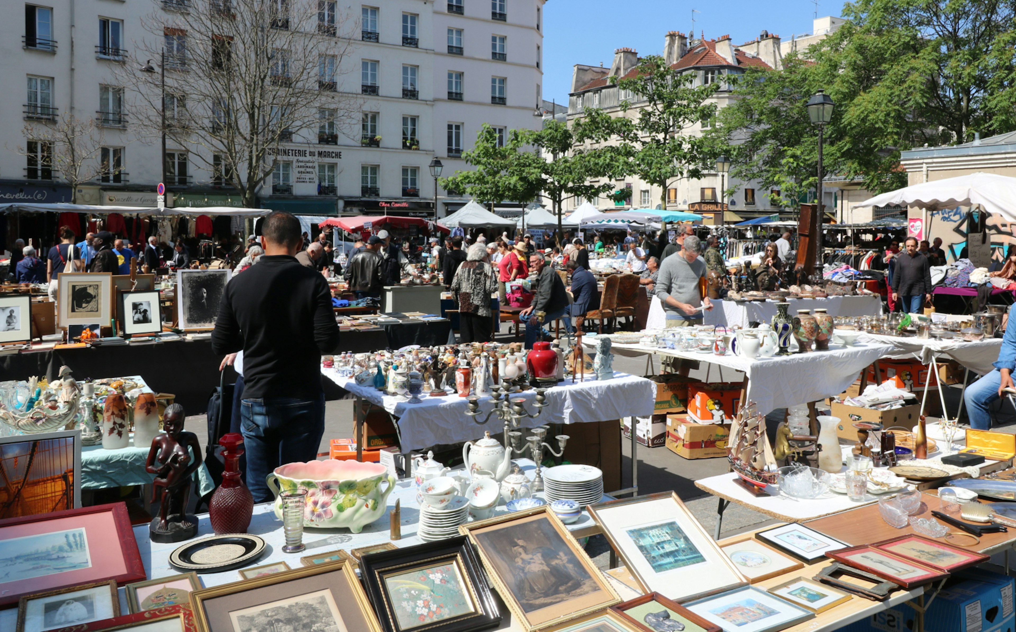 A Parisian flea market is drenched in sunshine; it's busy with people, and tables are lined with artwork and trinkets