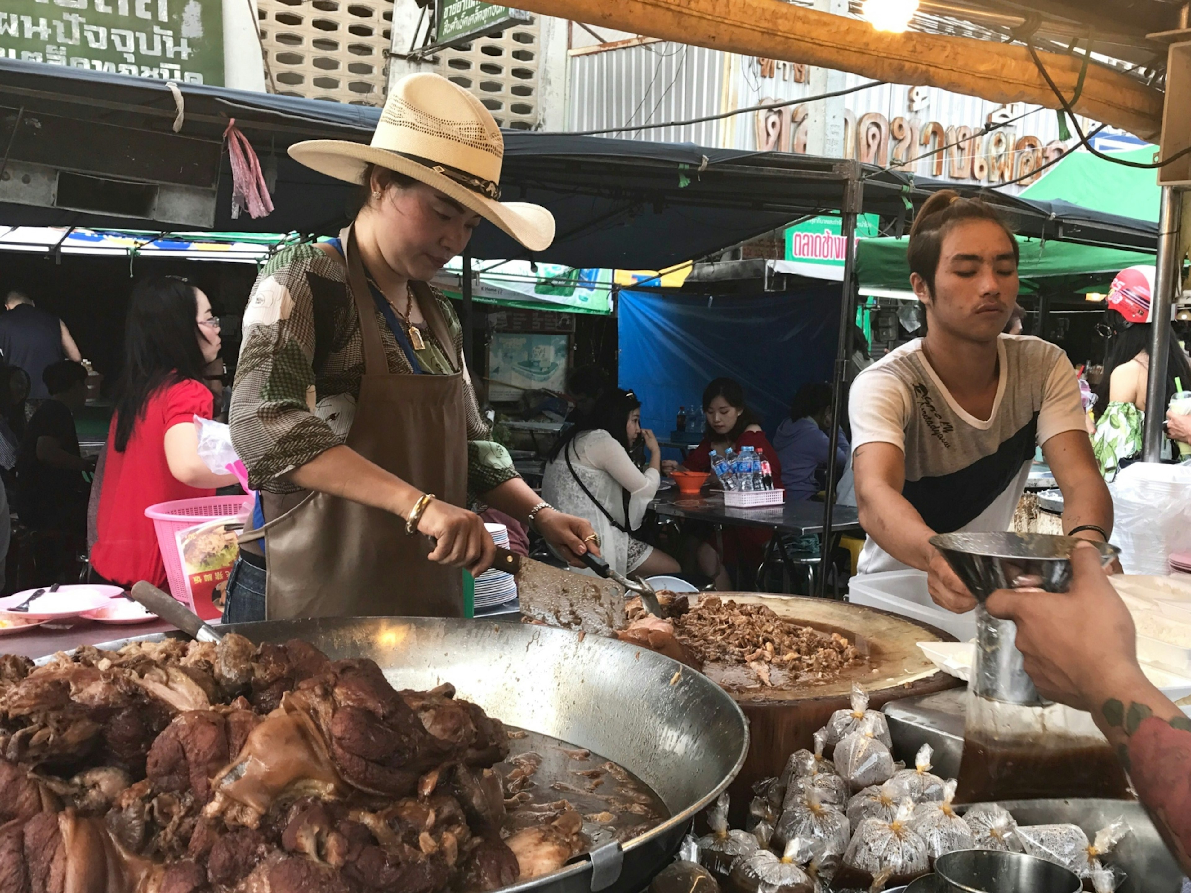 The famed 'Cowboy Hat Lady' serves slow-cooked pork leg to eager diners at Talat Pratu Chang Pheuak market in Chiang Mai © Celeste Brash / Lonely Planet