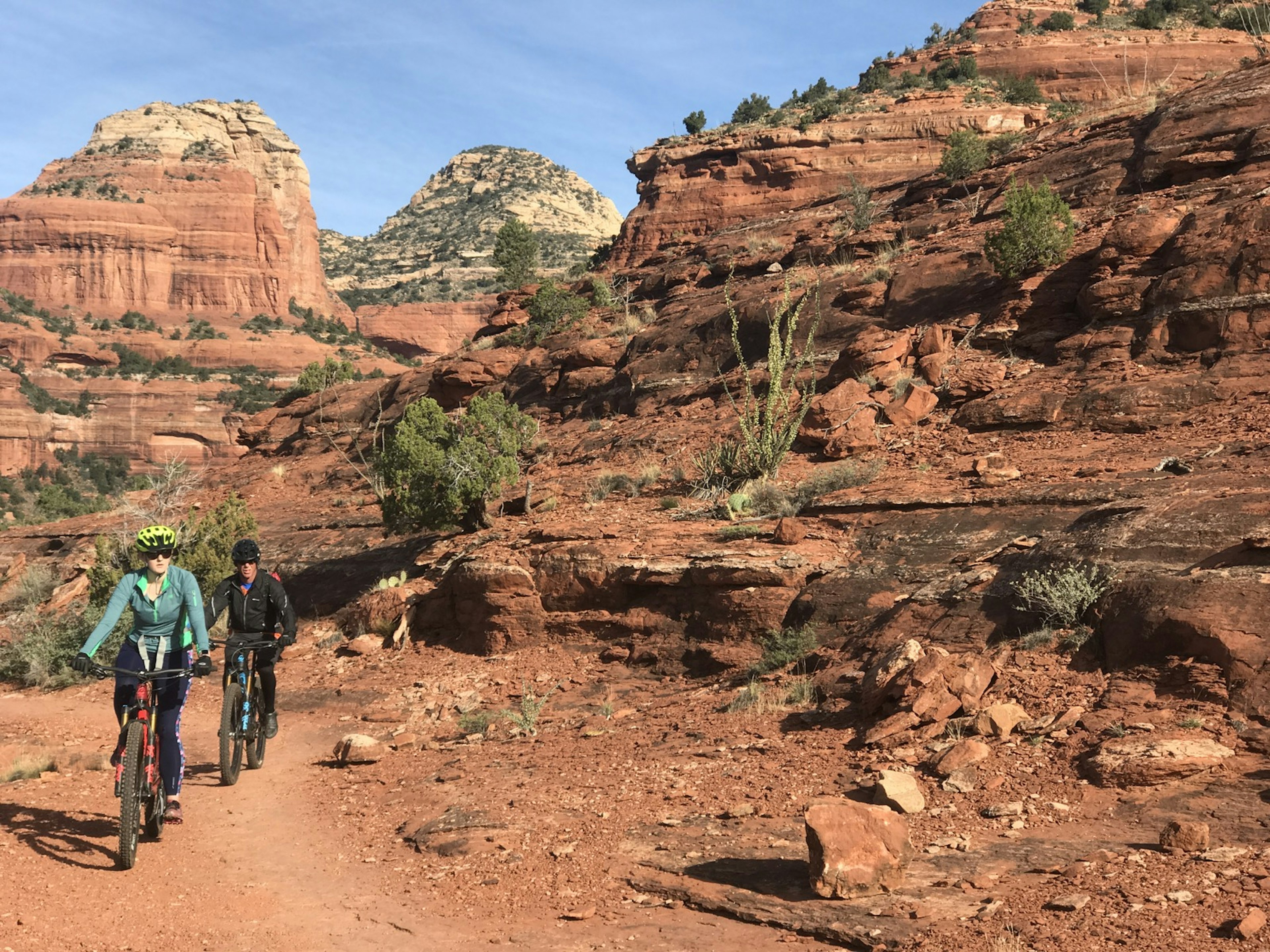 A female and a male ride mountain bikes on red rock formations in Sedona, Arizona.