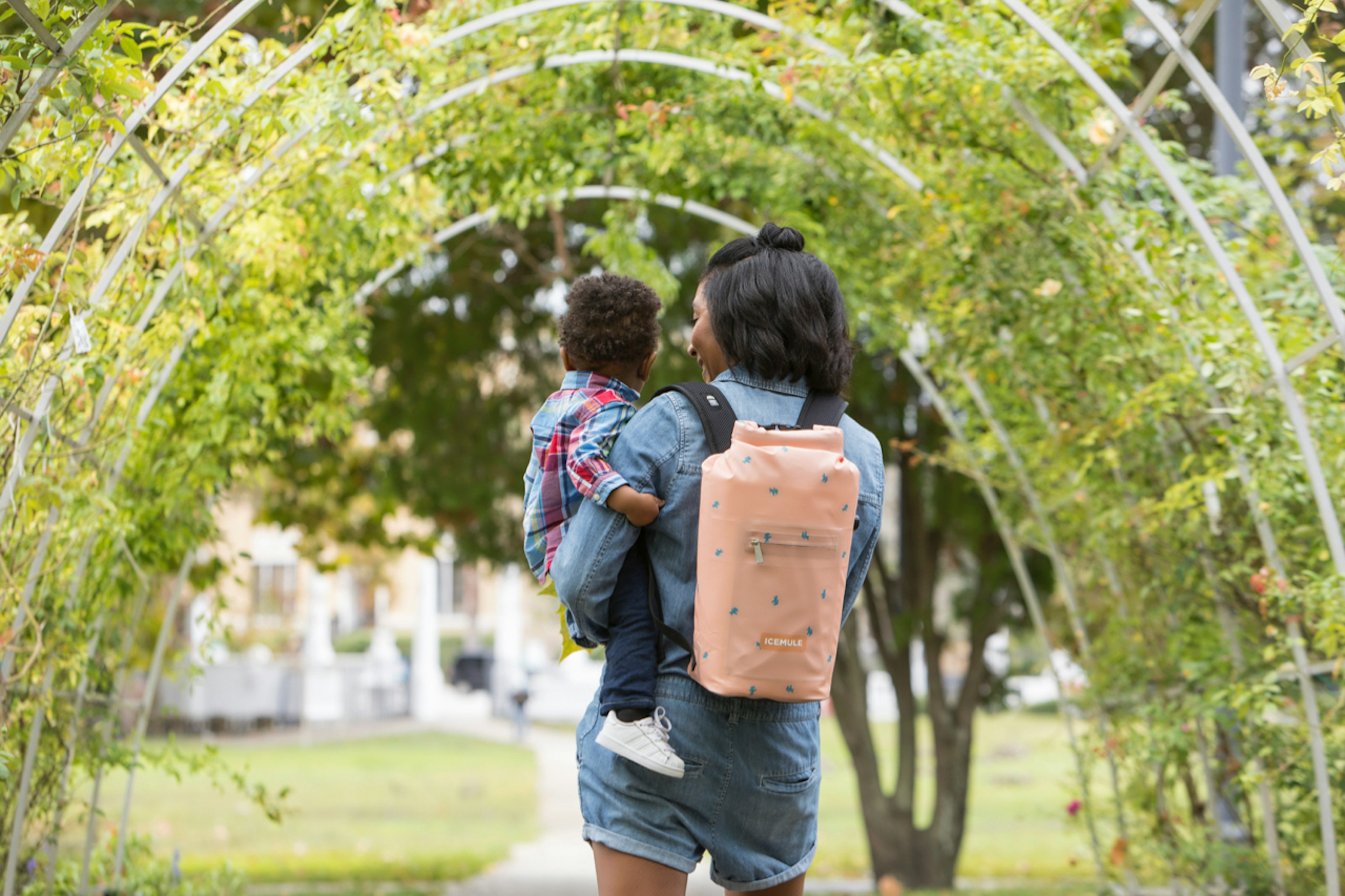 A woman wearing an IceMule Jaunt pink cooler and holding a baby