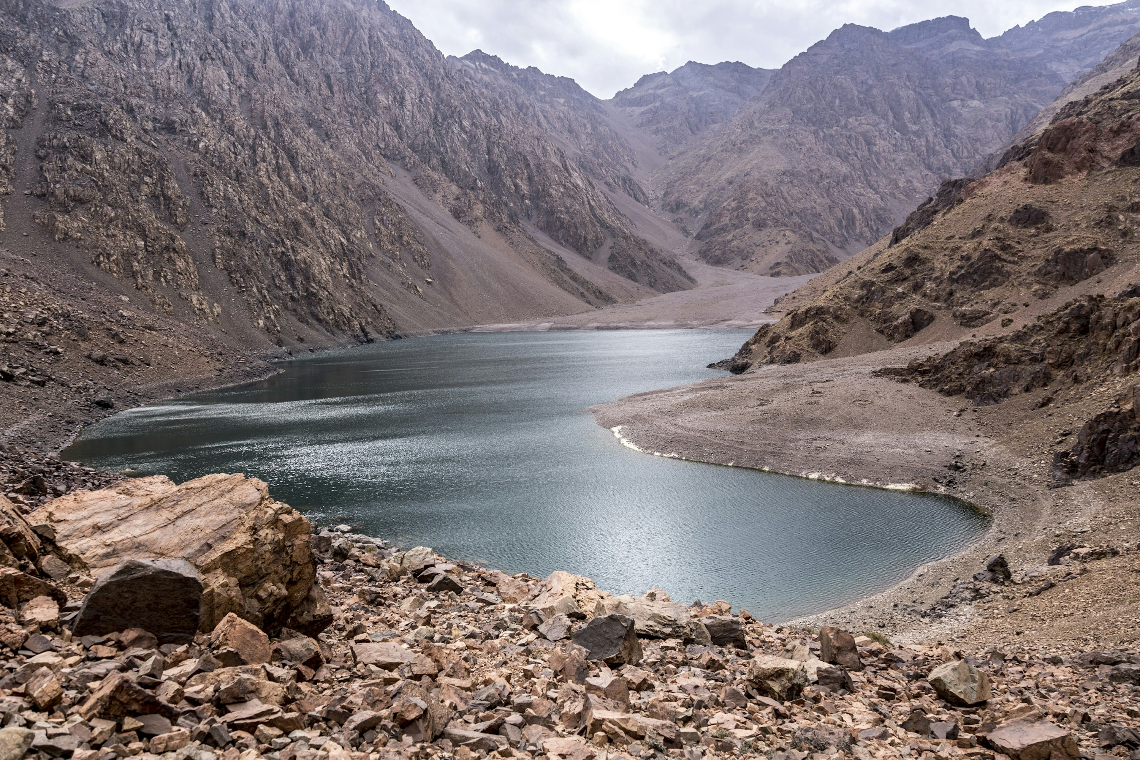 A kidney-bean-shaped lake sits at the bottom of rugged rock and scree slopes; there is no vegetation in sight whatsoever.