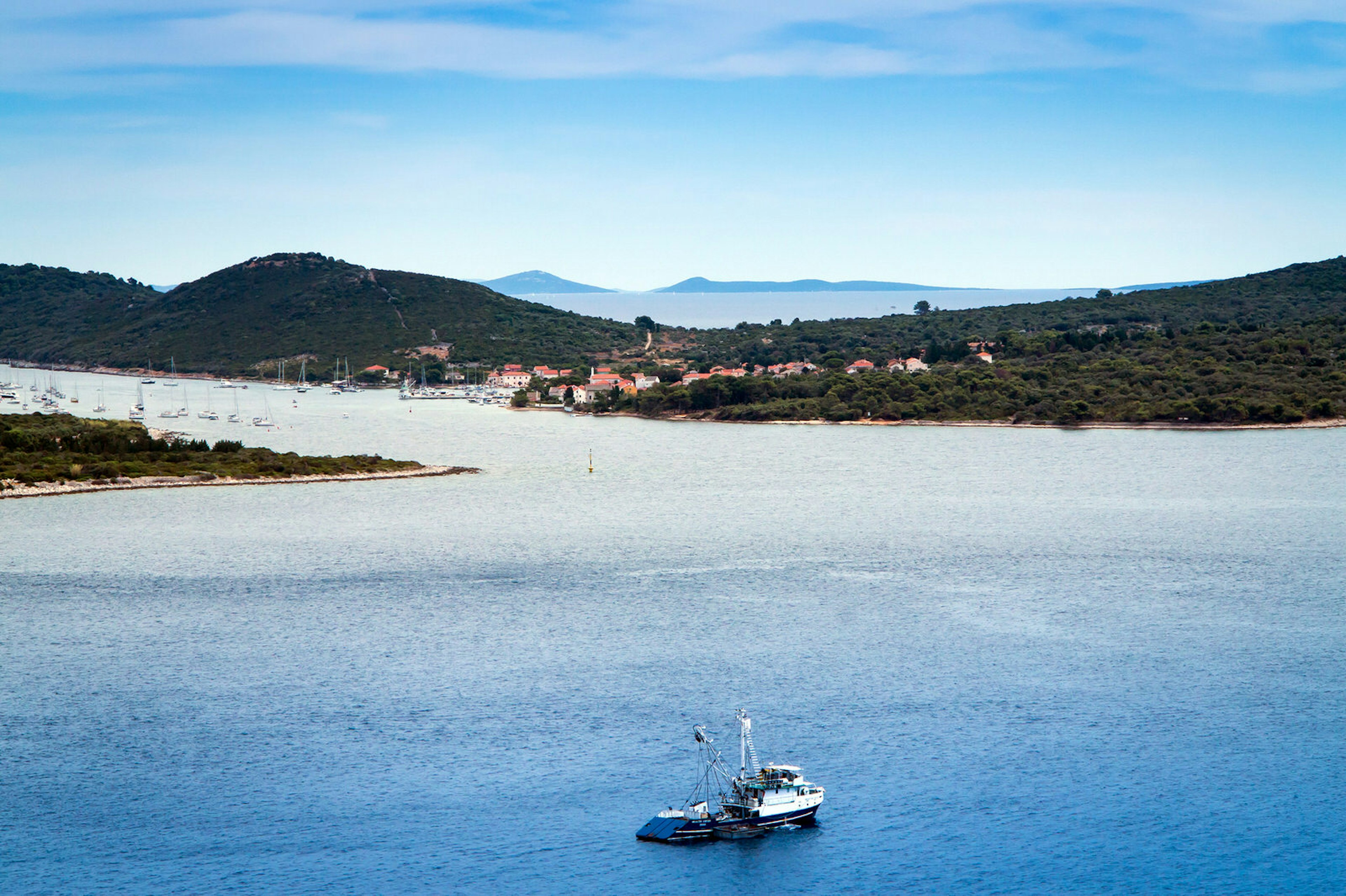 A view of Ilovik city and island, Croatia on a sunny day. A small fishing boat is heading towards the island which is covered in dense greenery.