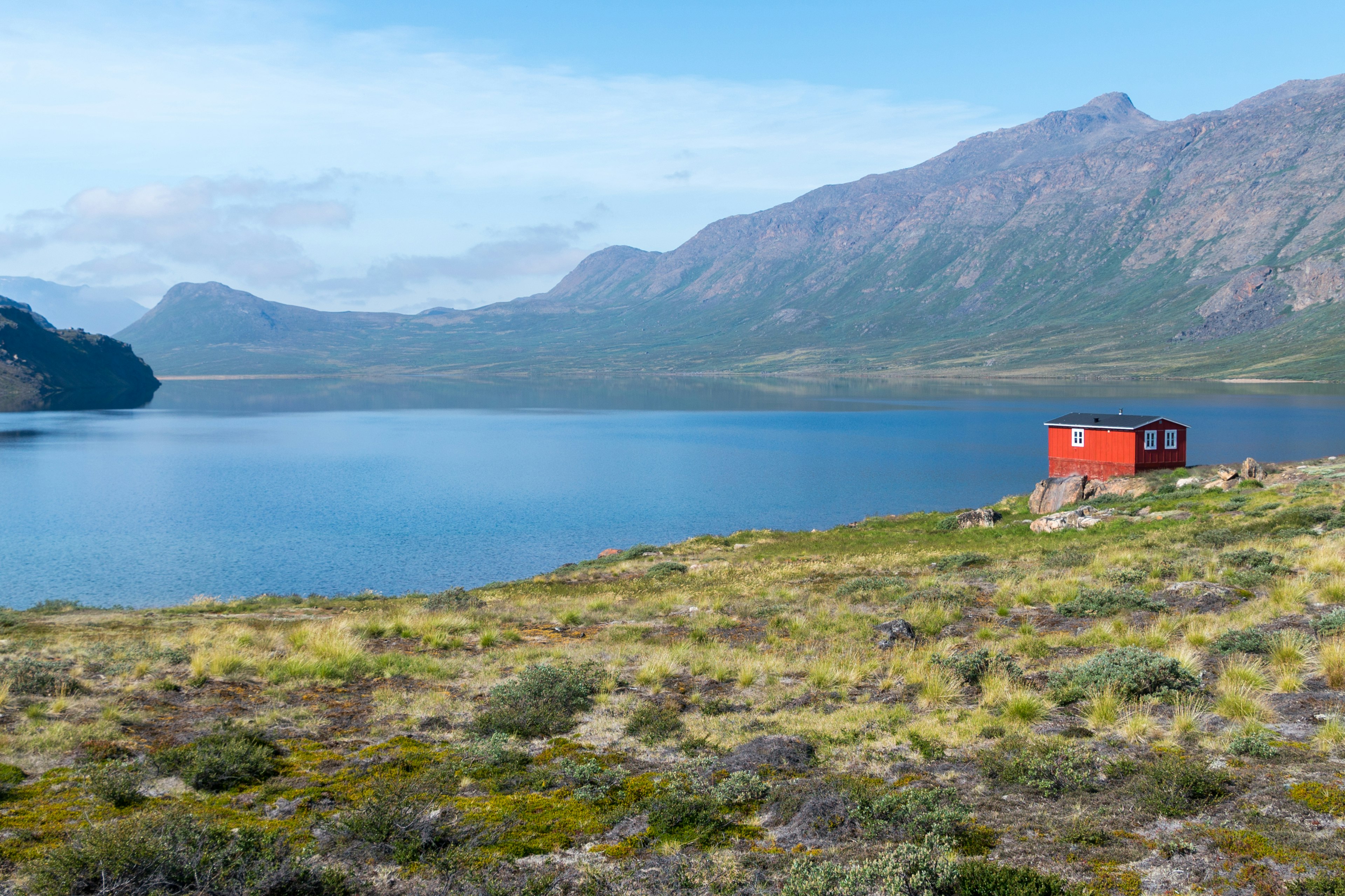 A red lakeside hut with mountain scenery beyond.