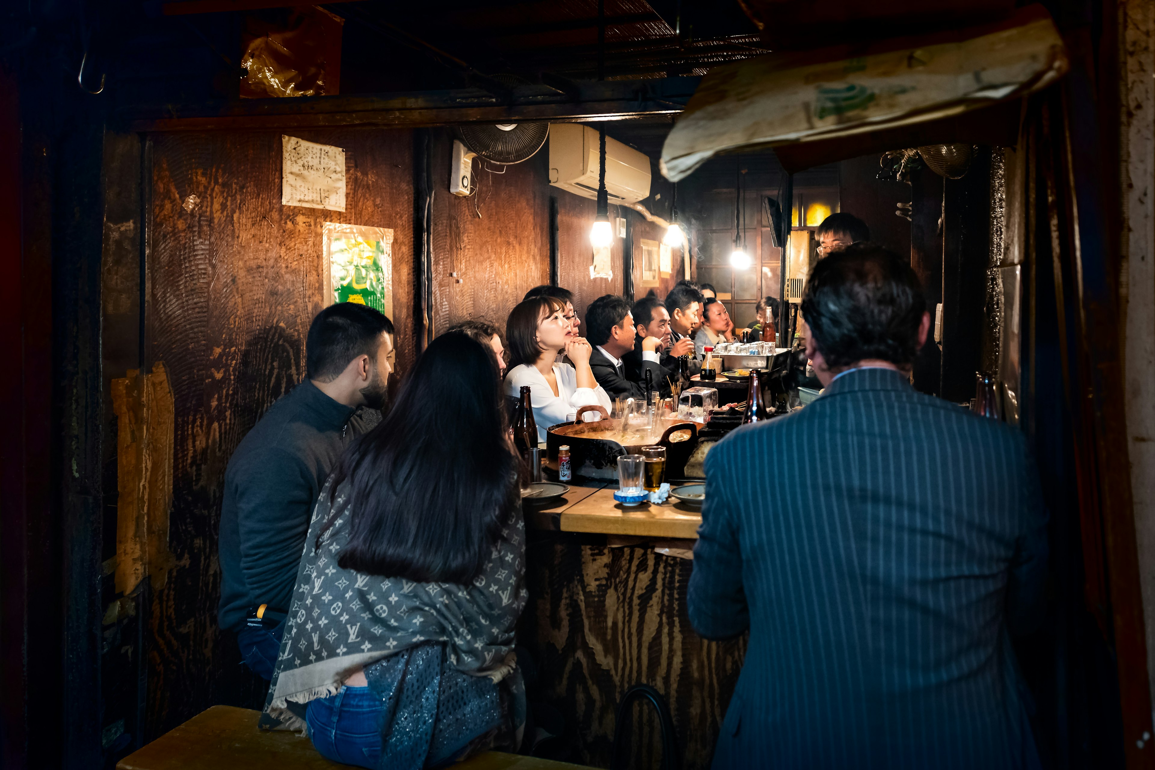 Memory lane alley with izakaya and people sitting, drinking and eating by sidewalk in Tokyo city at night, chef cooking yakitori grilled chicken food