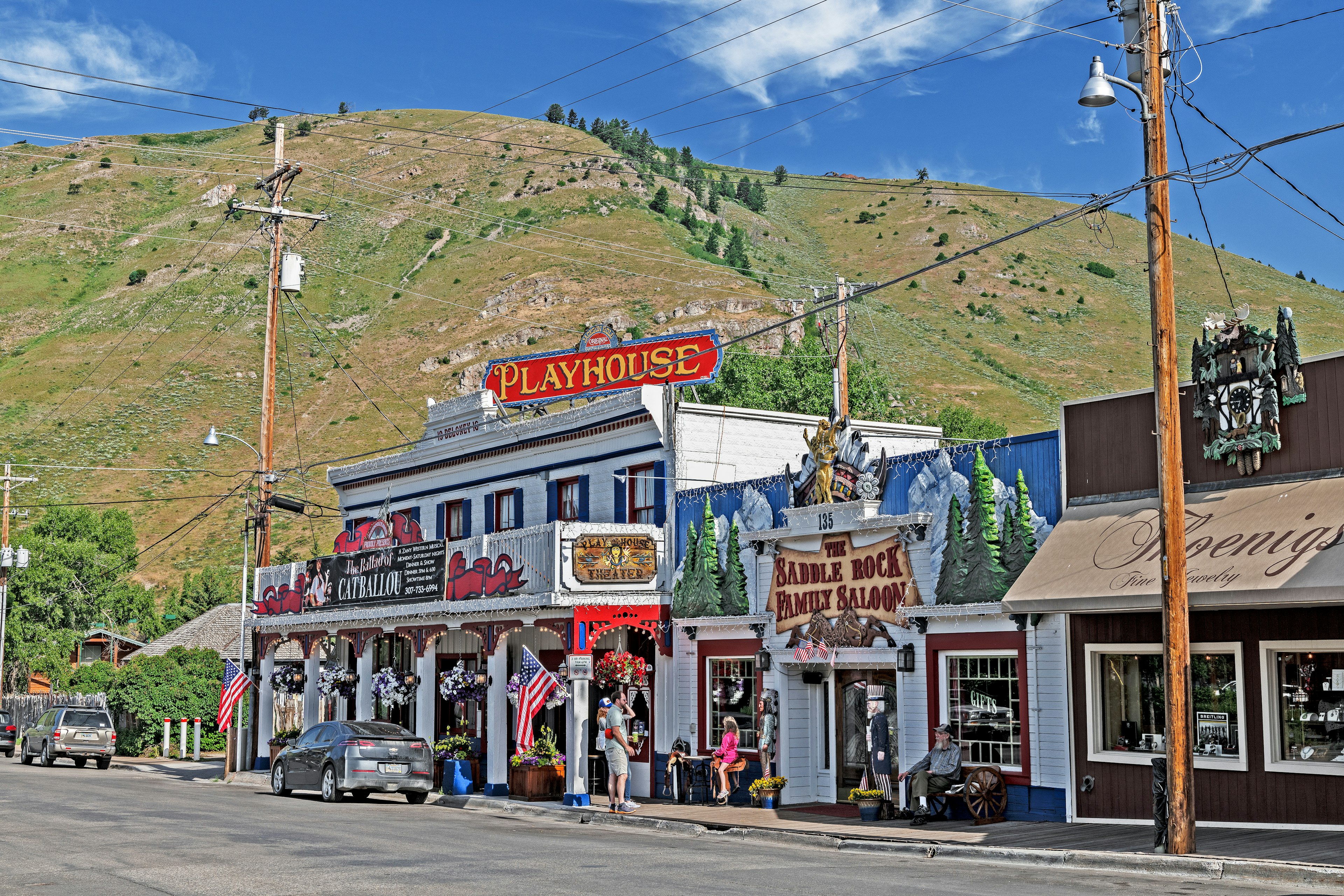 Exterior view of Jackson Hole Playhouse is an old western-style saloon. There is a large green hill in the background.