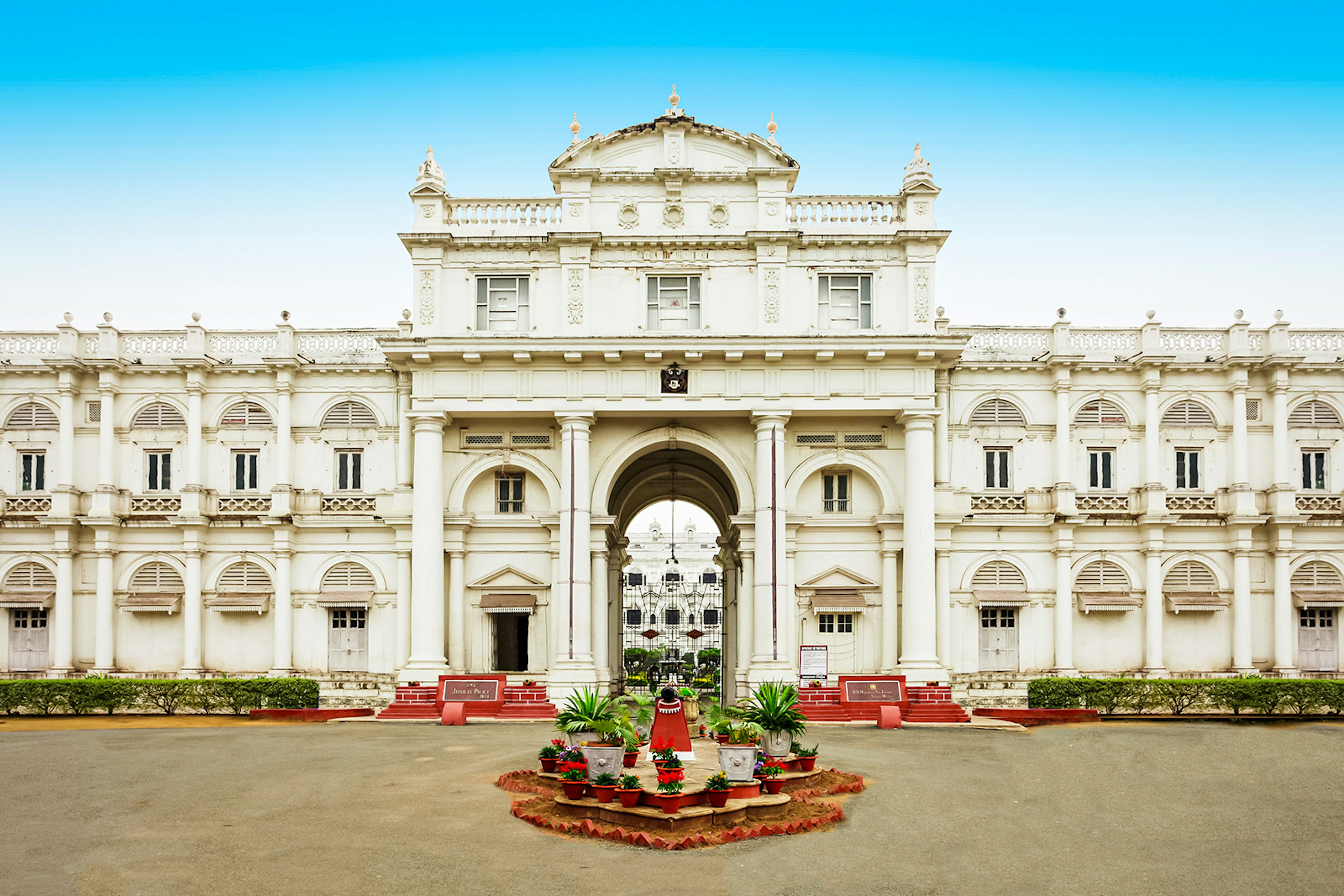 The entrance of the white Jai Vilas Palace; the exterior is covered in columns and arches, and a small garden sits in the foreground. Madhya Pradesh, India.