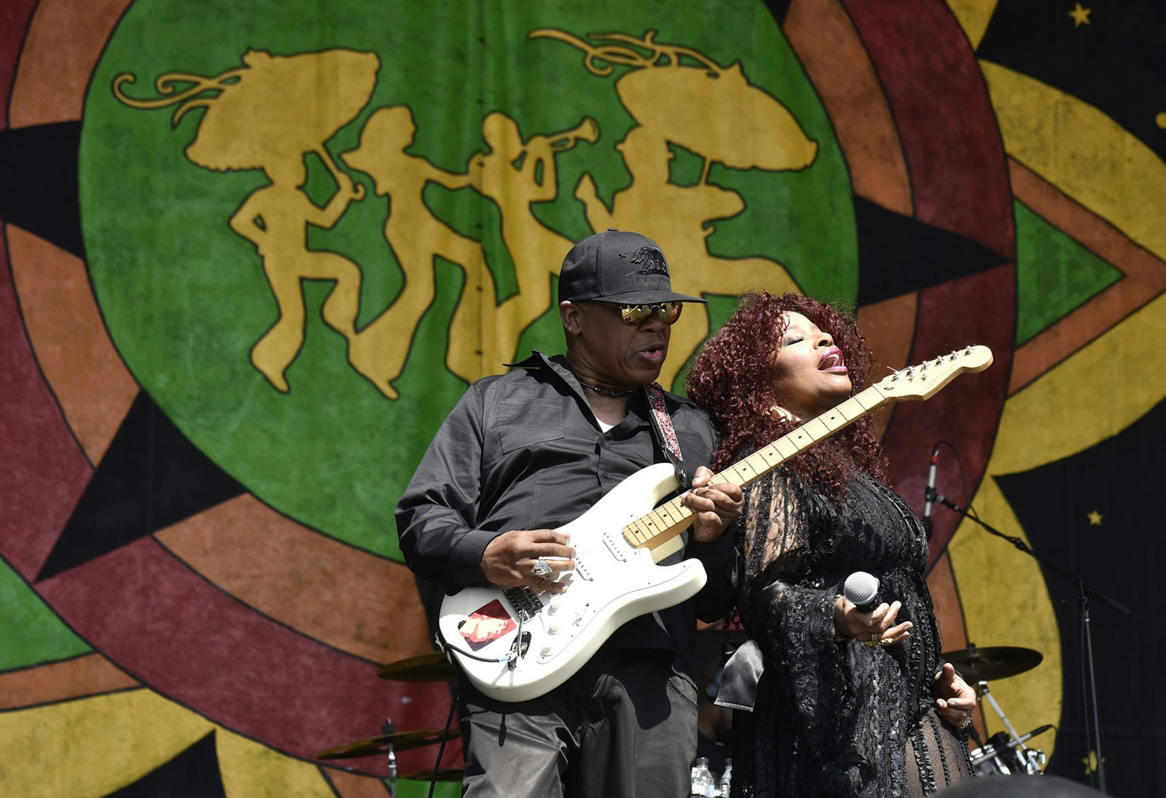 Disco legend Chaka Khan leans back against a man playing the electric guitar as she sings in front of a large tapestry; New Orleans Festivals