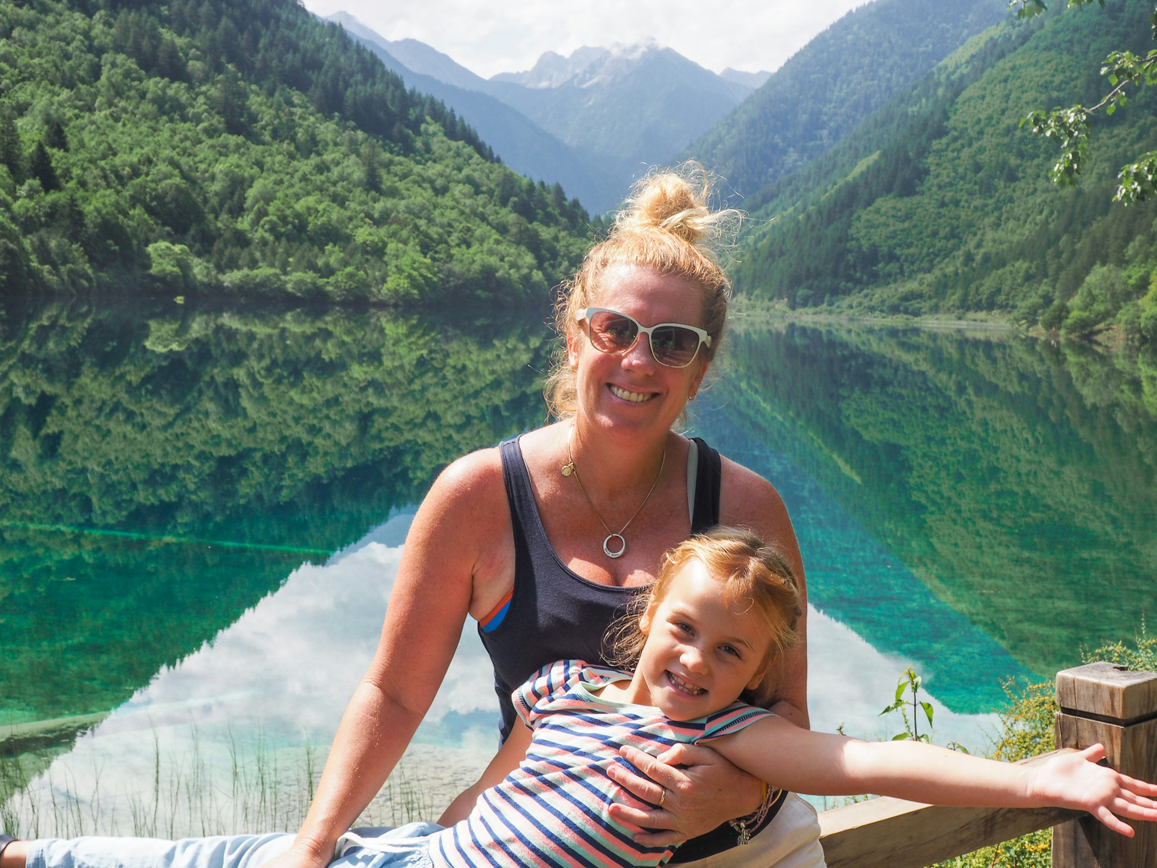 Evie and Emmie posing for a photo on the shores of a lake surrounded by lush forests in Jiuzhaigoa, China.