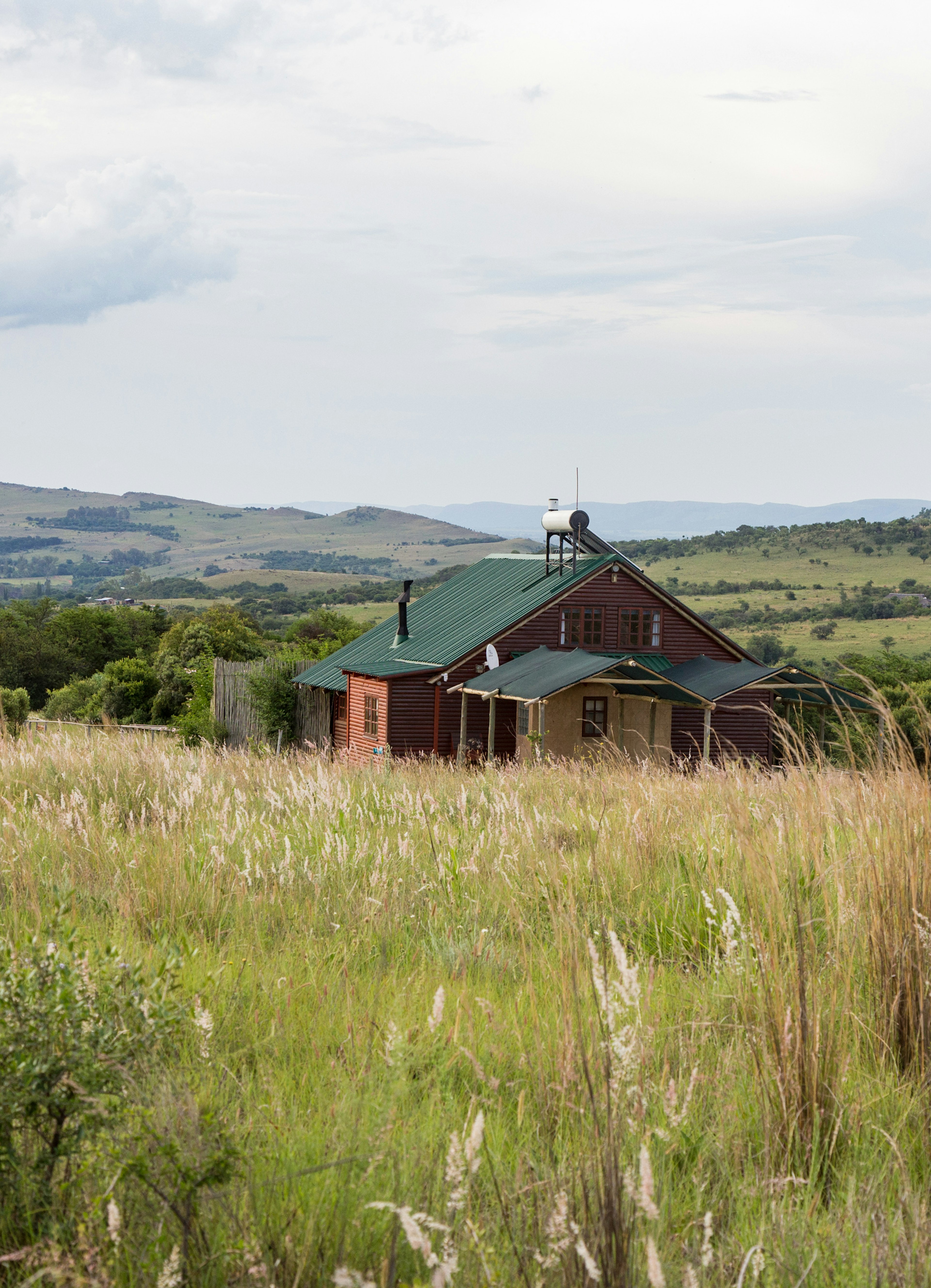 Stone Hill, a petite wooden cottage sits nestled in long grass with the rolling hills around Magaliesburg.