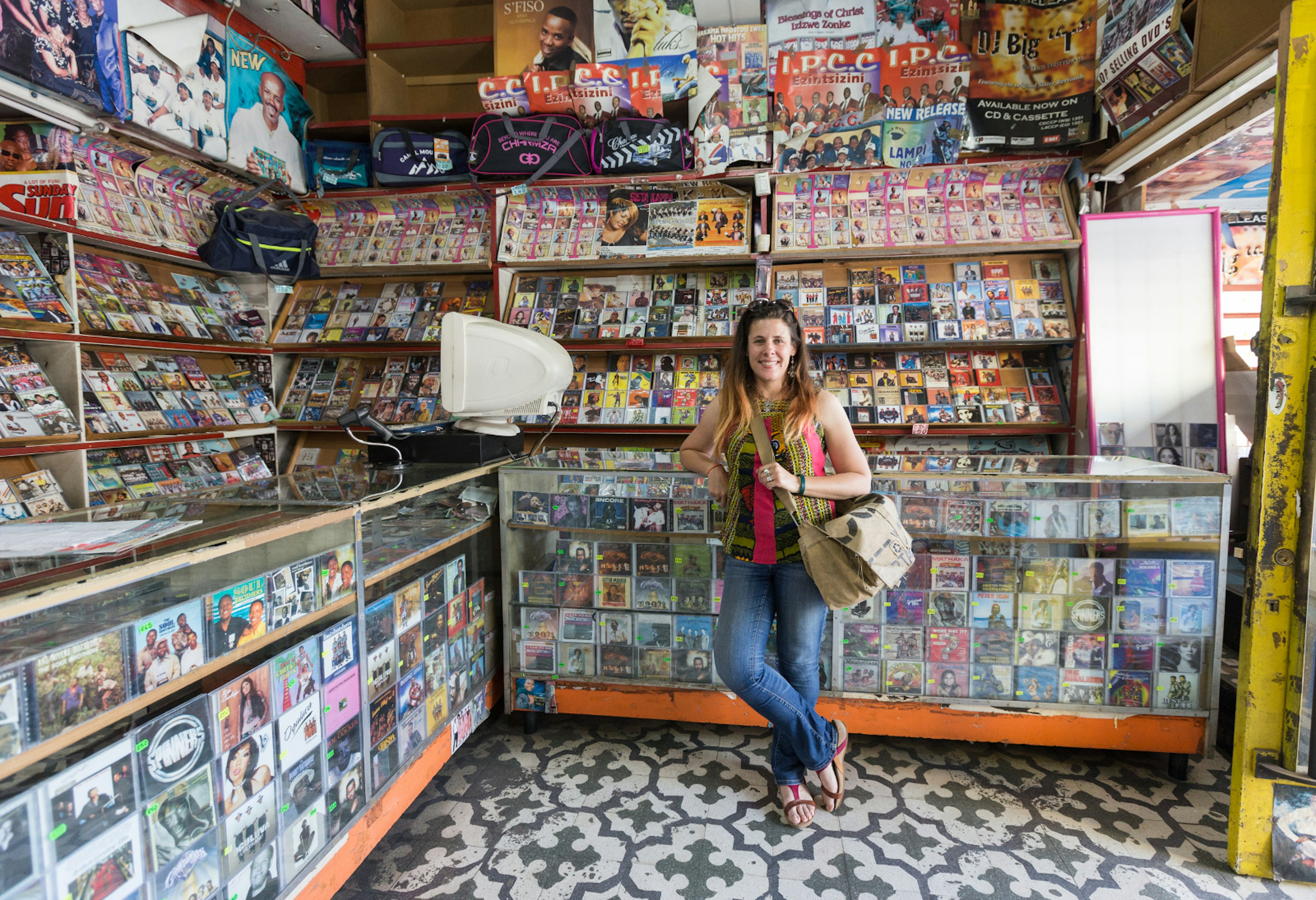 The writer Heather Mason stands smiling and surrounded by cds and cassettes in the Vinyl Joint on Eloff Street, downtown Johannesburg.